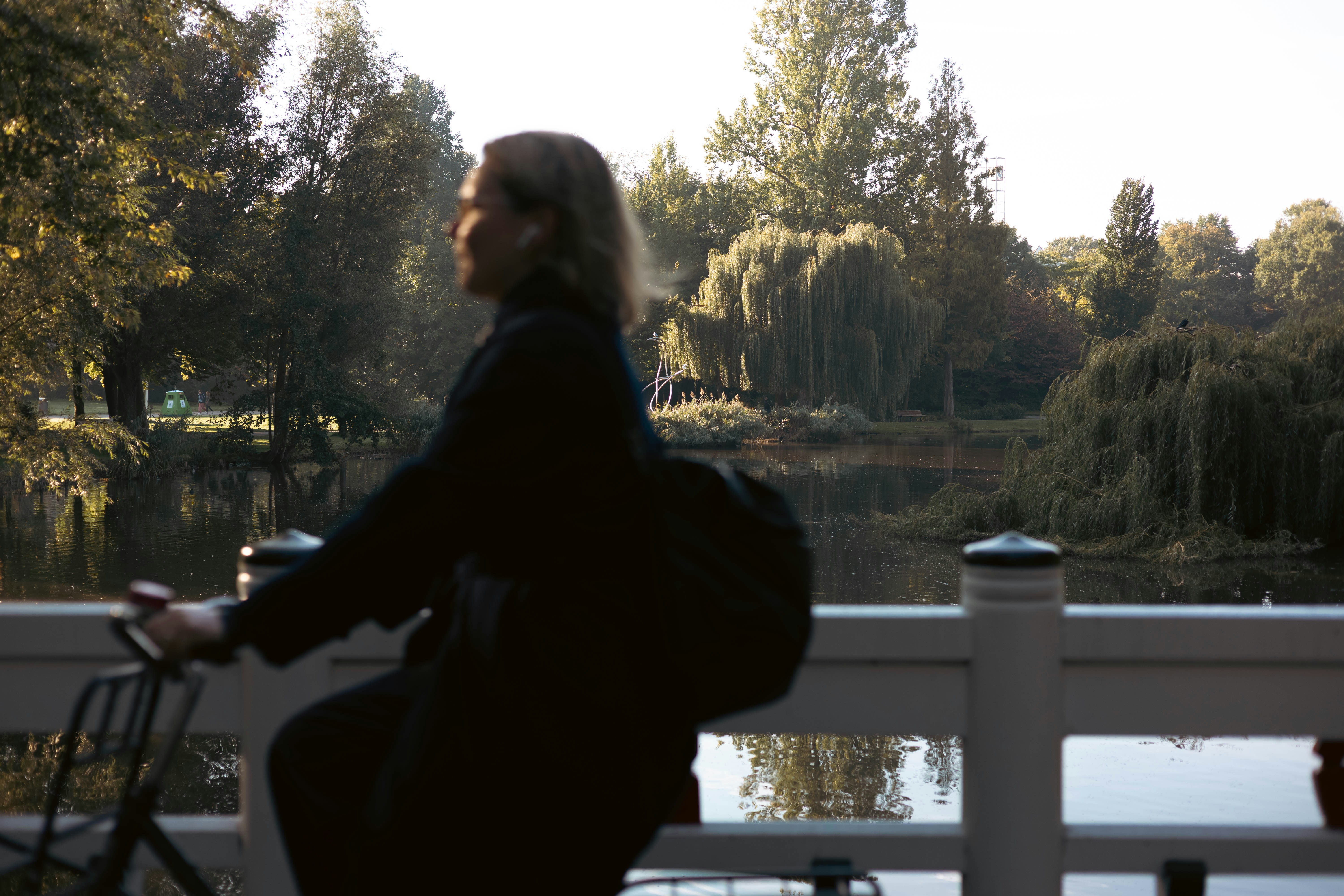 Woman cycling on a bridge by a tranquil lake.