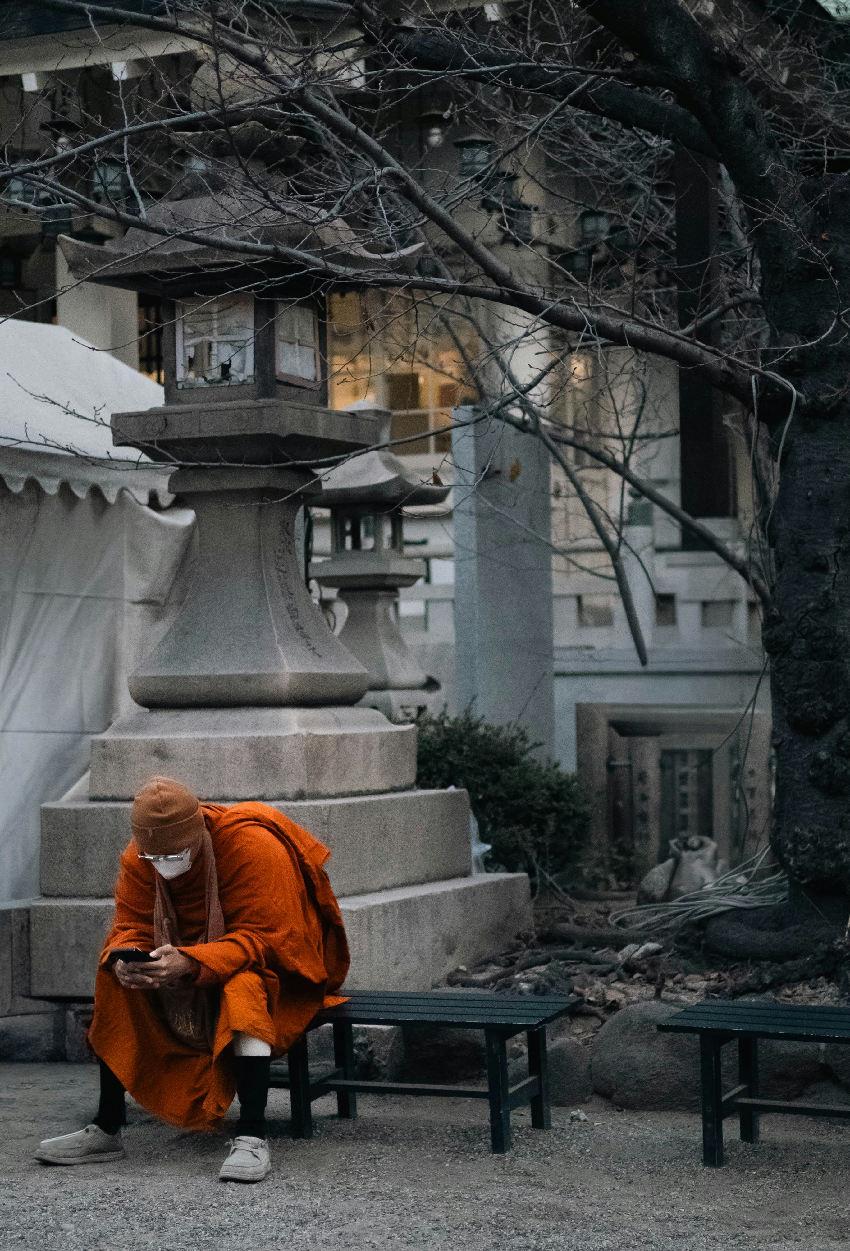 Monk in orange robes sits using a smartphone.
