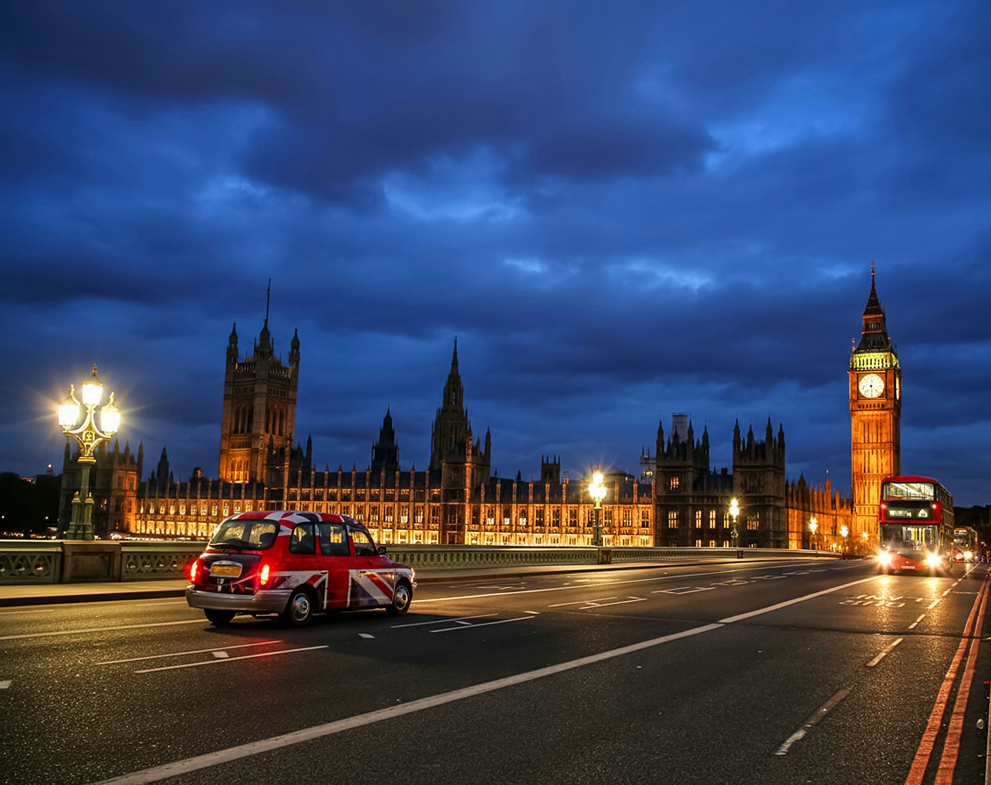 A london taxi and bus at dusk near parliament.