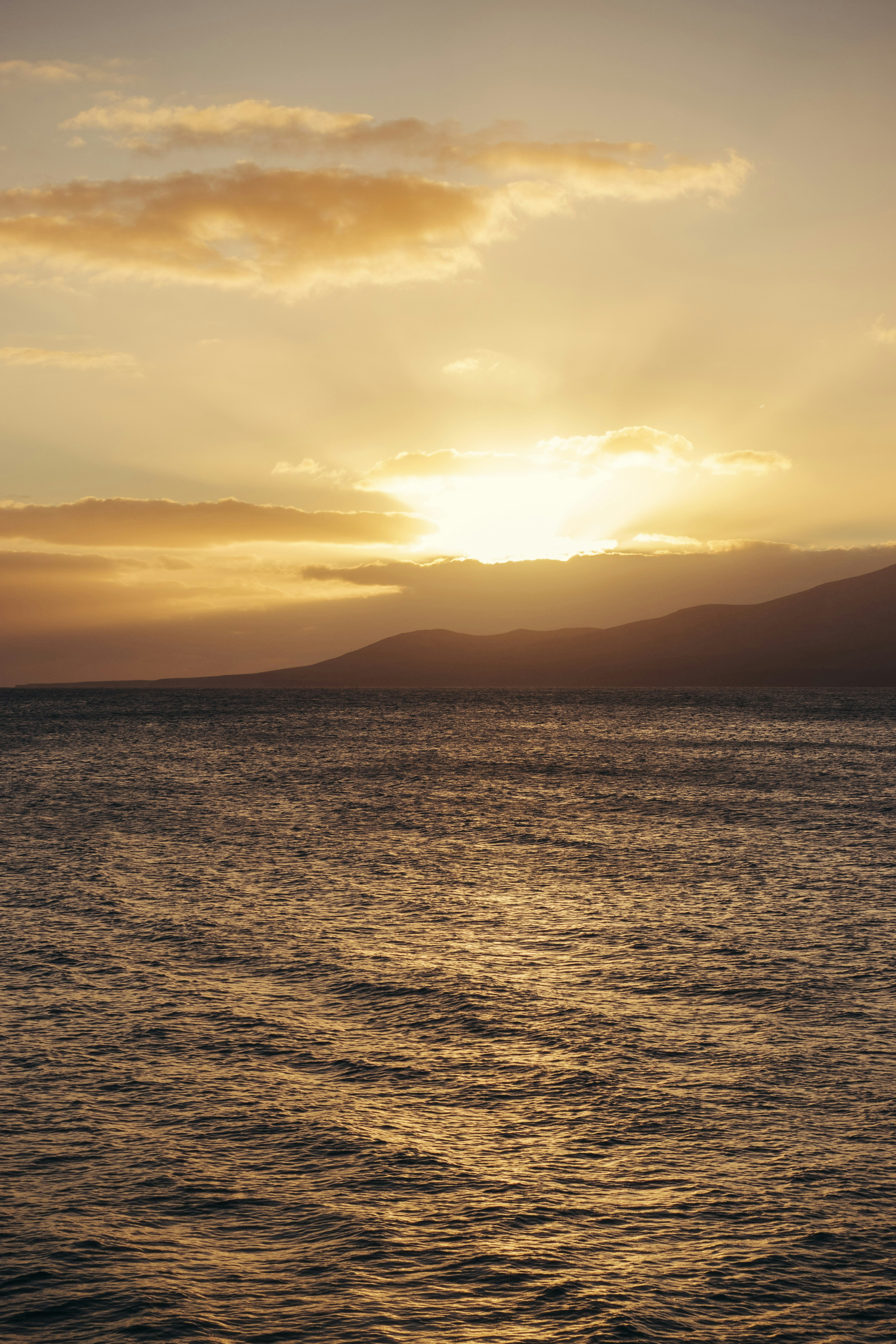 Golden sunset over the ocean with distant hills.