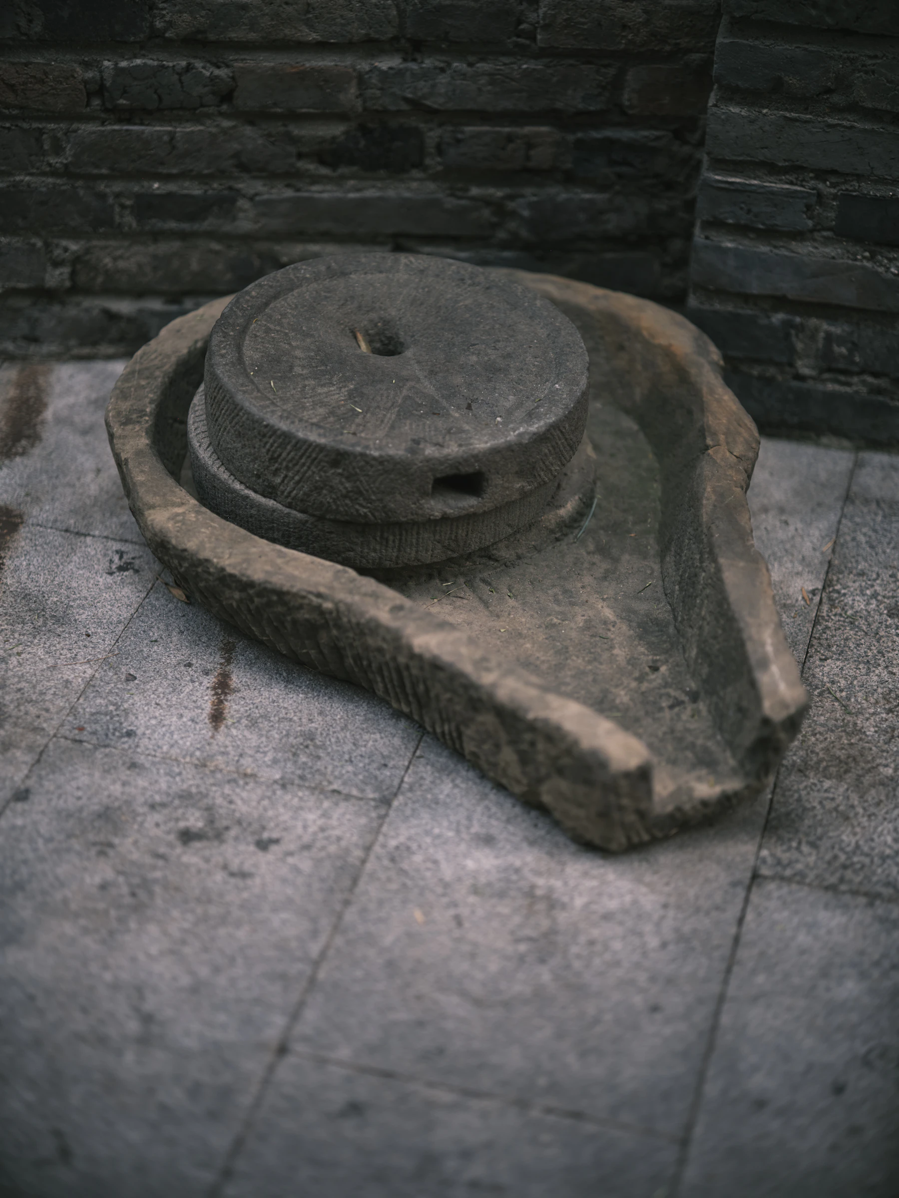 An old hand quern: two grooved round millstones resting in a carved stone basin on a tiled floor