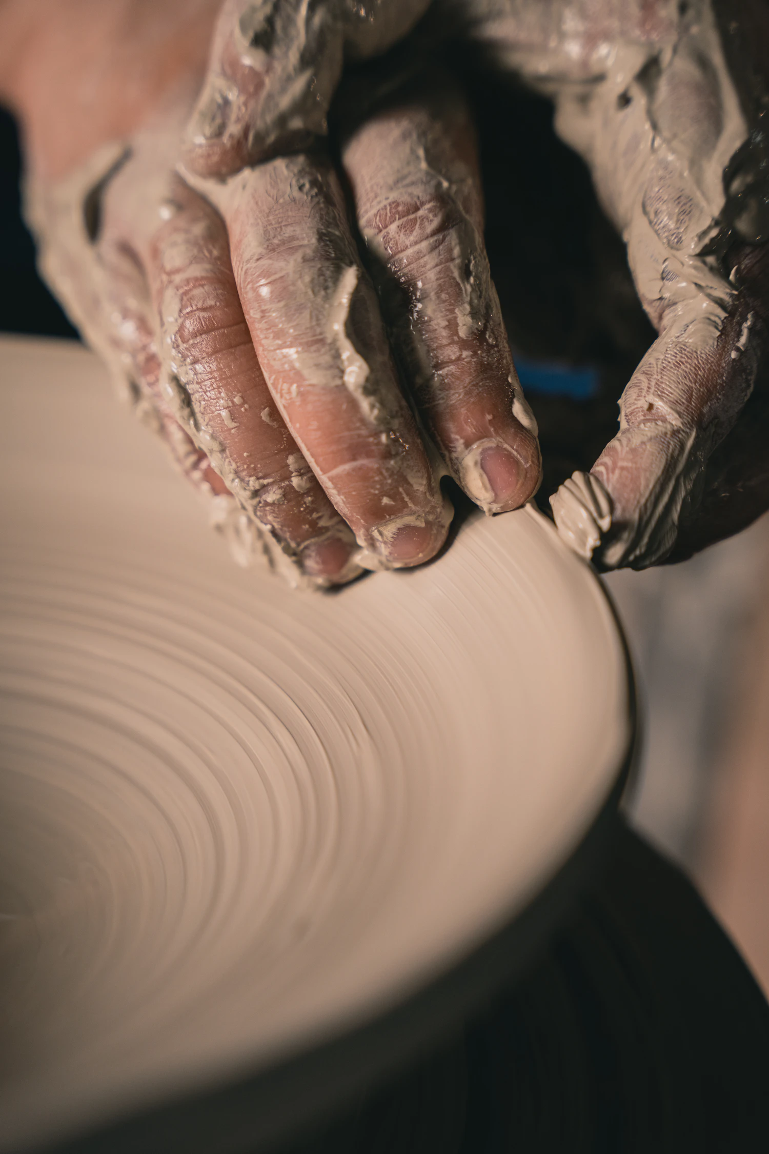 Hands covered in wet clay shaping the rim of a pot
