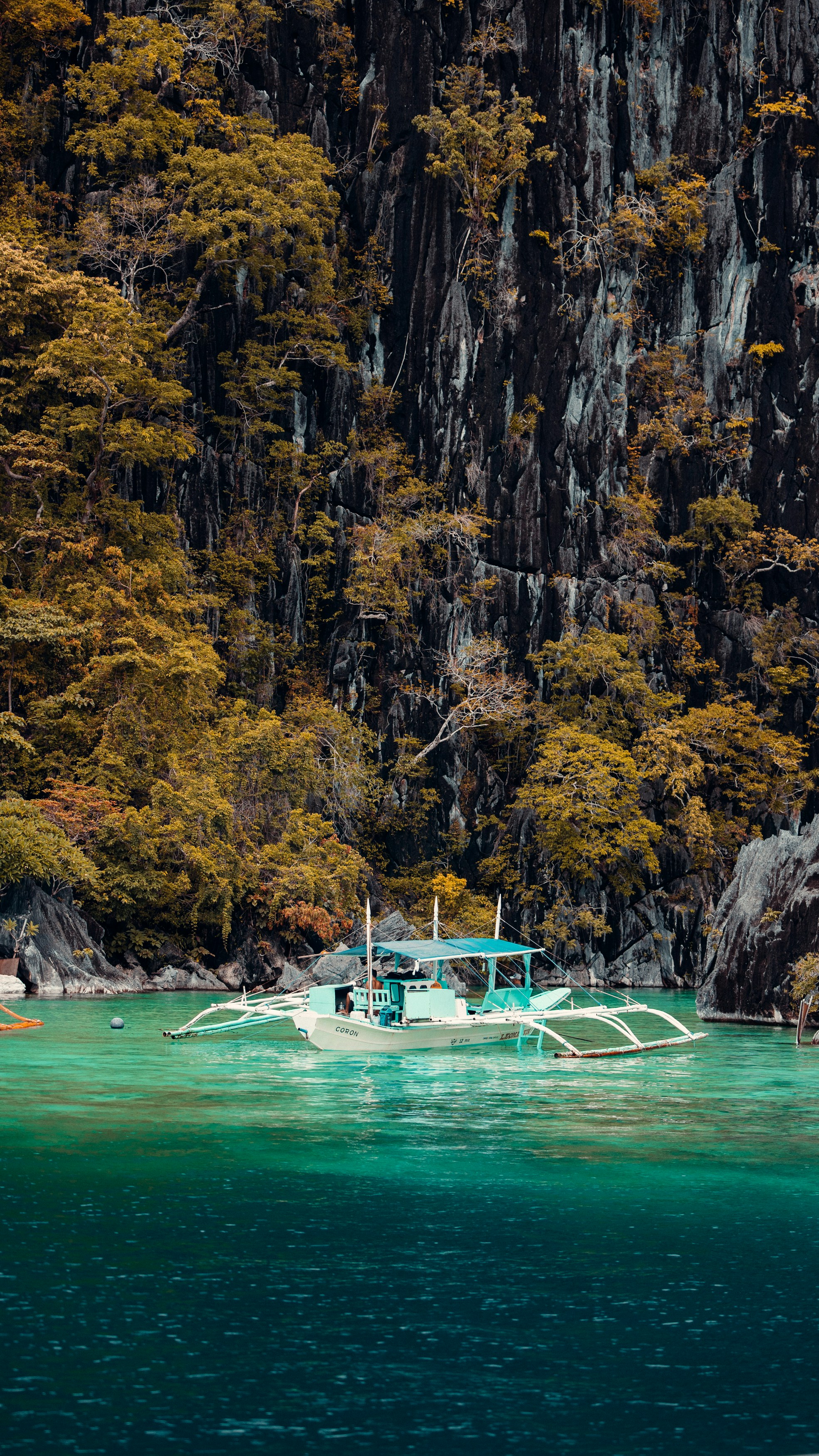 A traditional boat floats on turquoise water near cliffs.