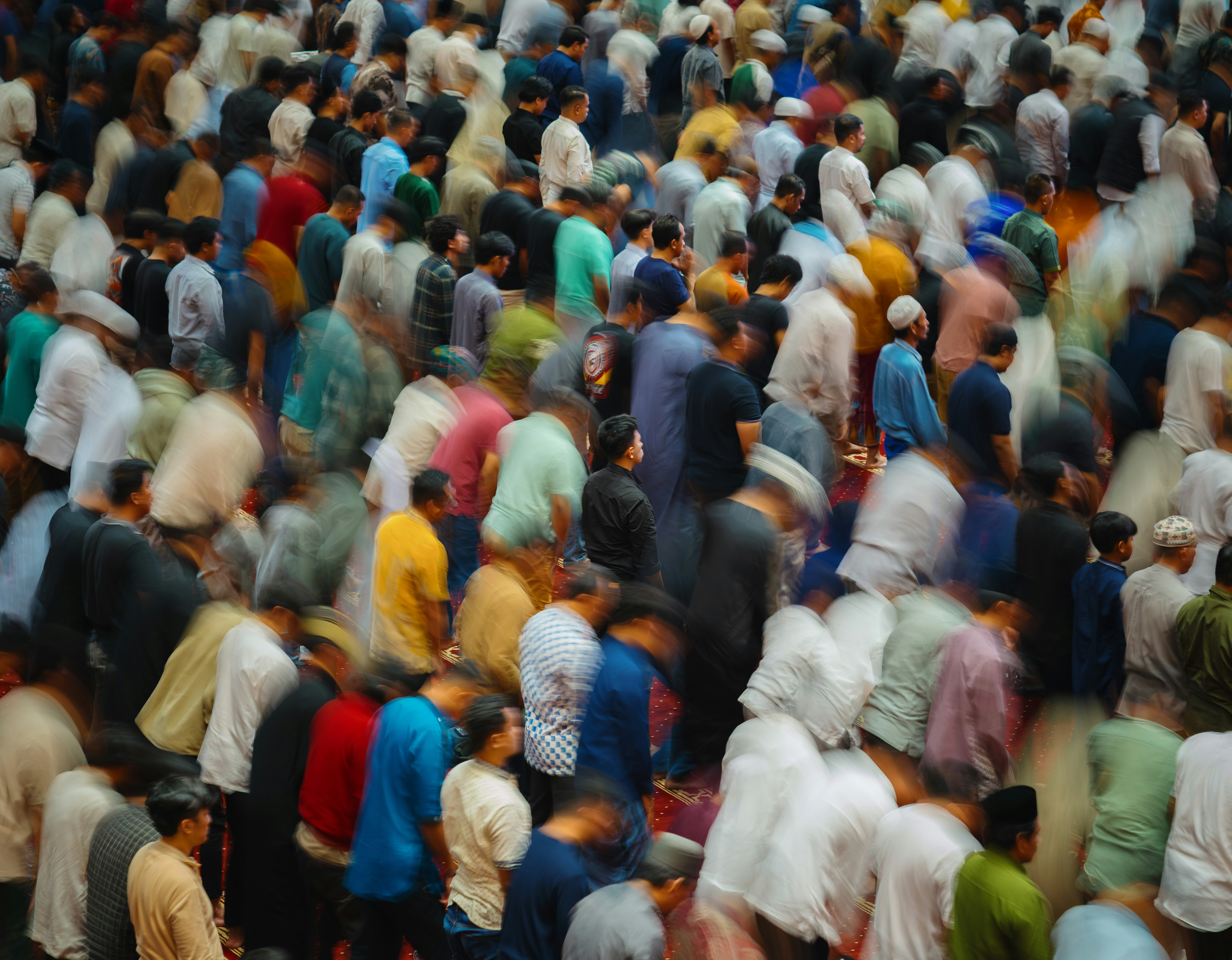 A blurred crowd of people praying together outdoors.