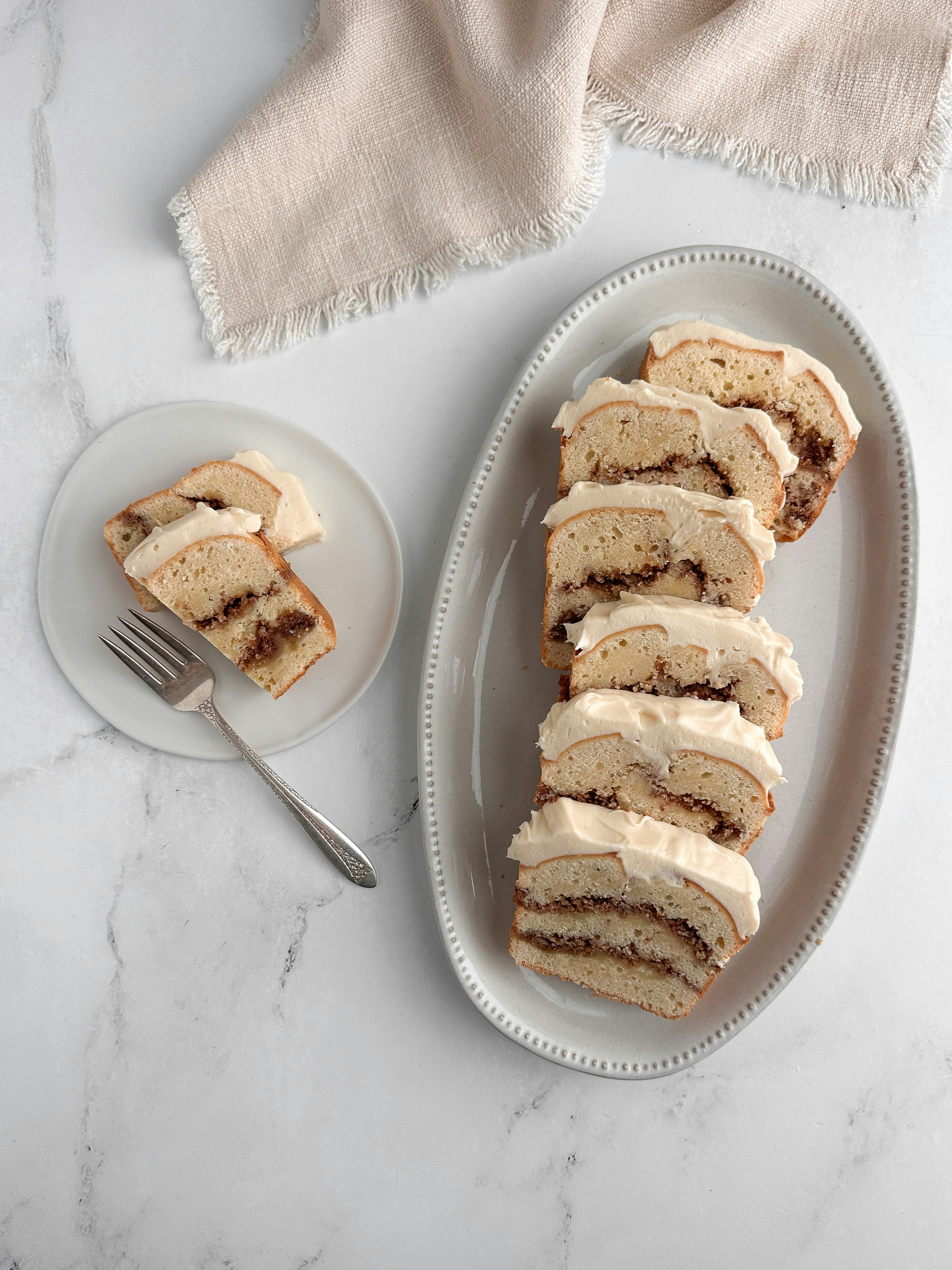 Sliced cinnamon roll cake with frosting on platter.