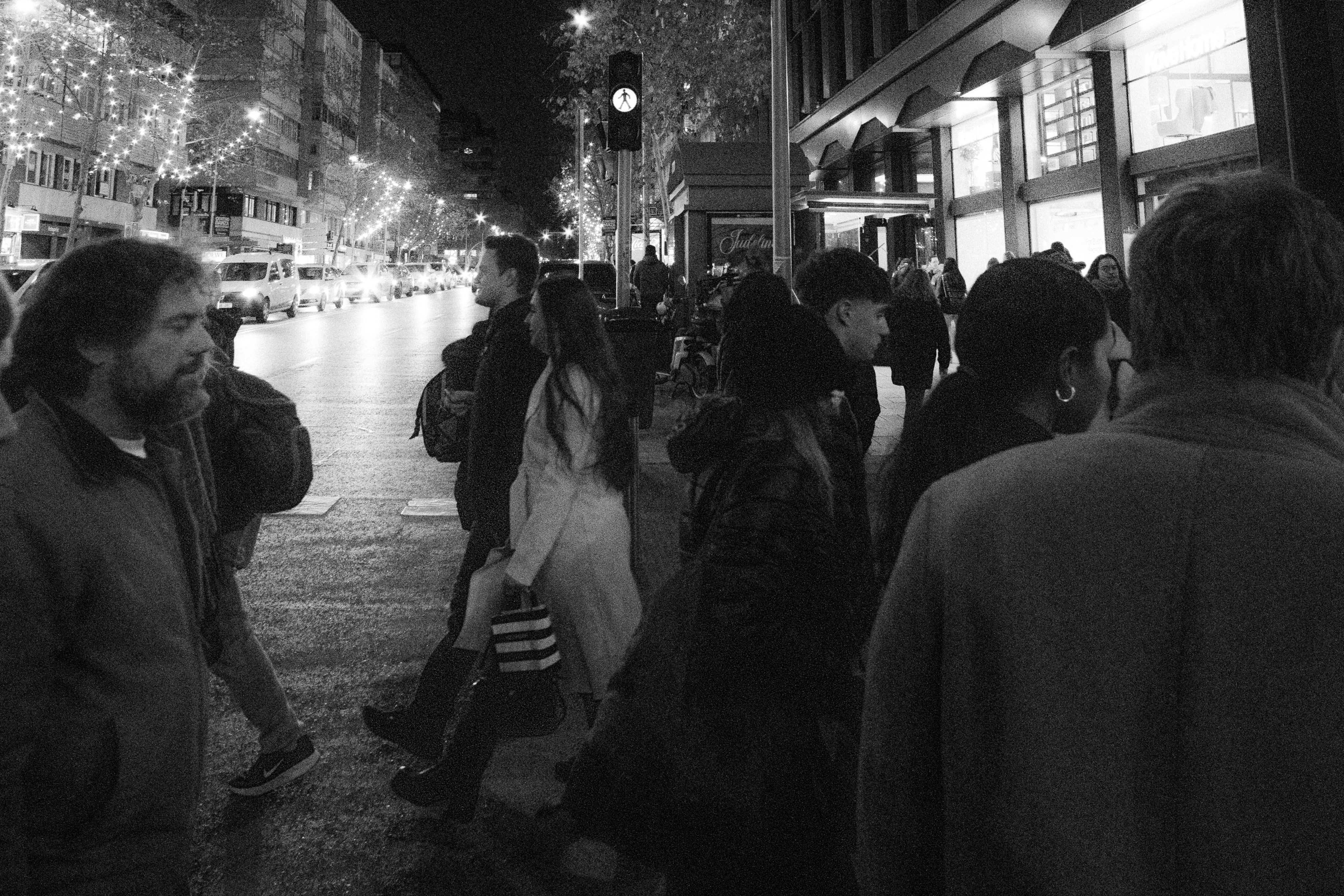 People crossing a street at night with city lights.