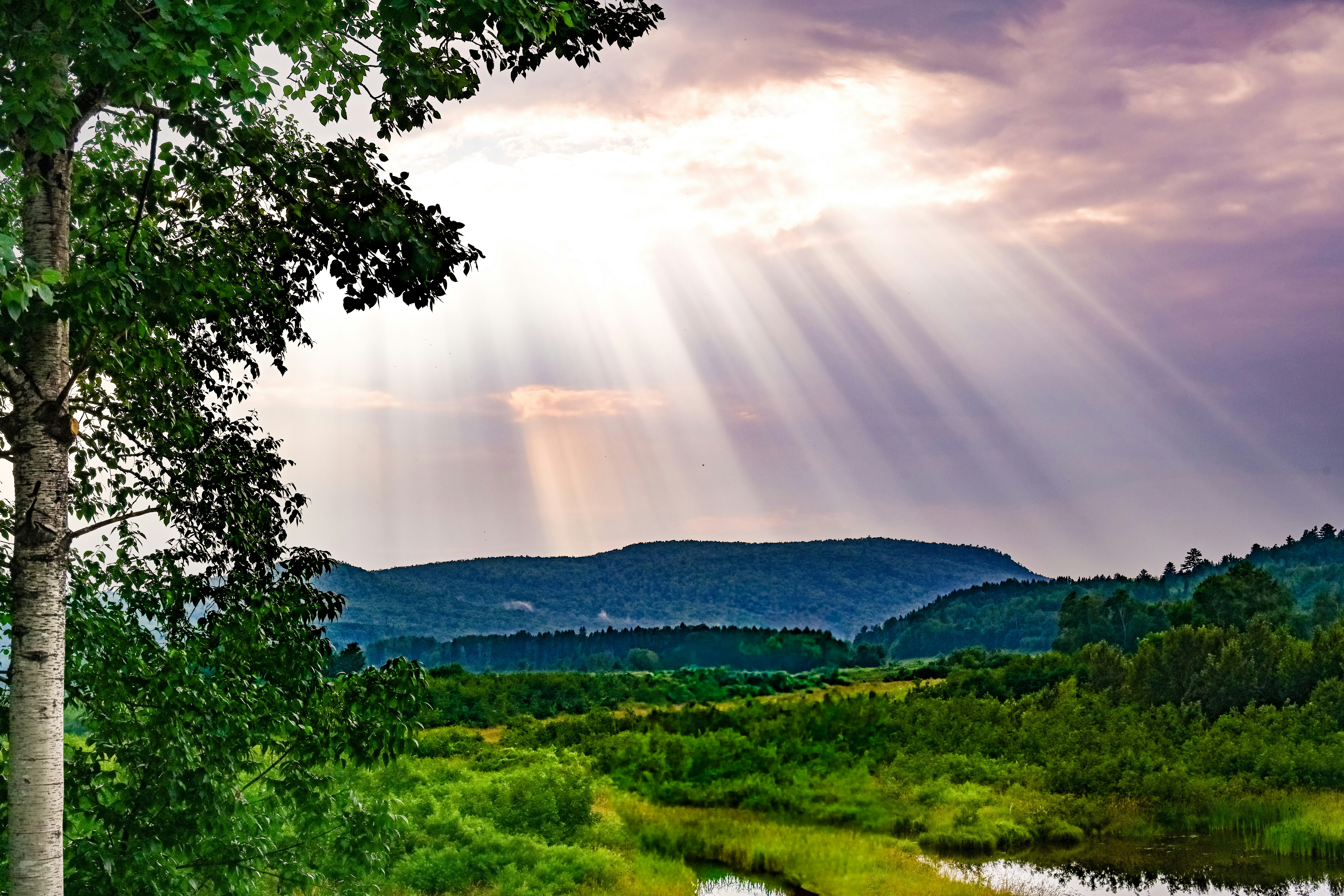 Sunbeams shine through clouds over rolling hills.