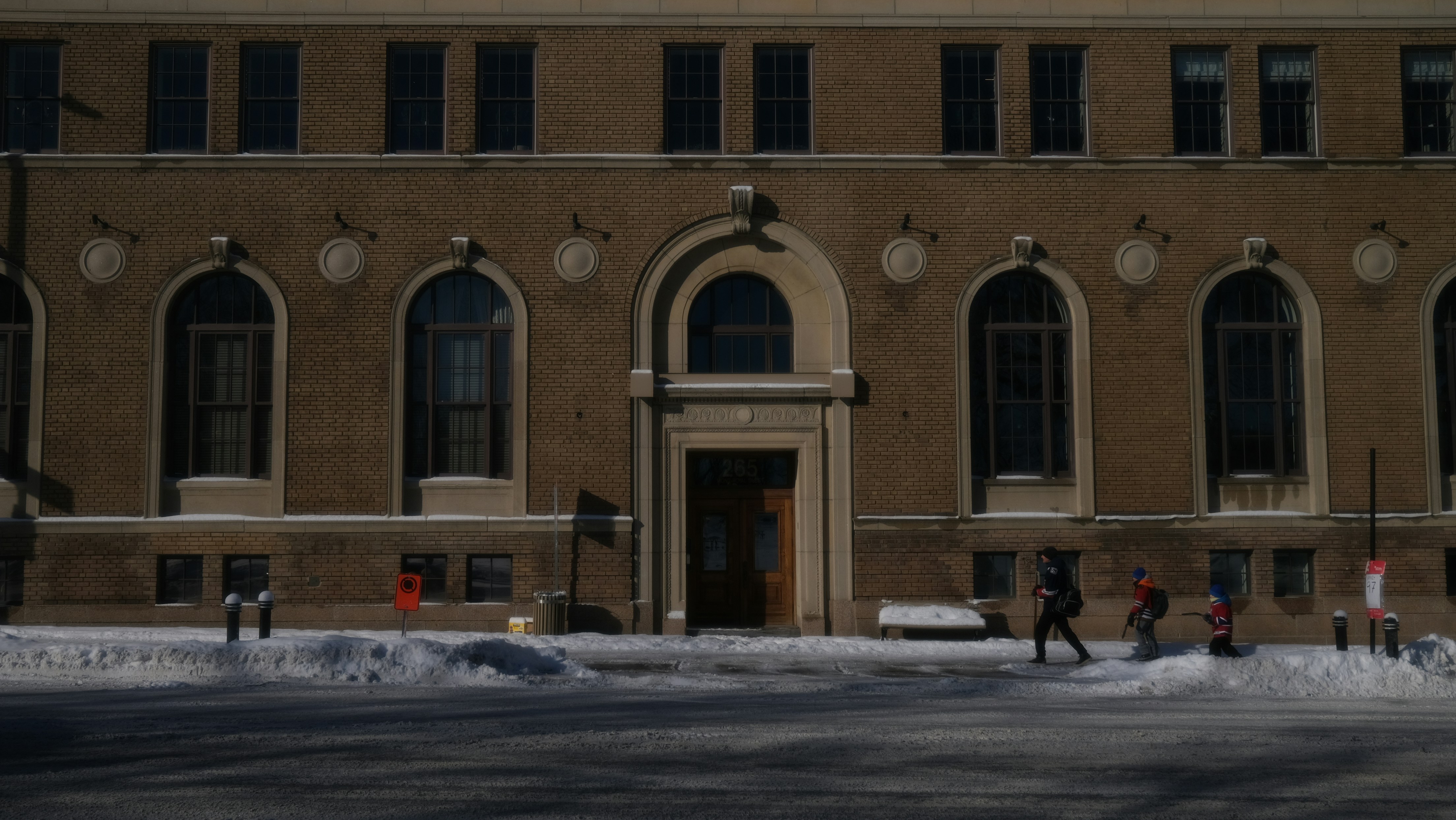 People walk past a building with arched windows in snow.