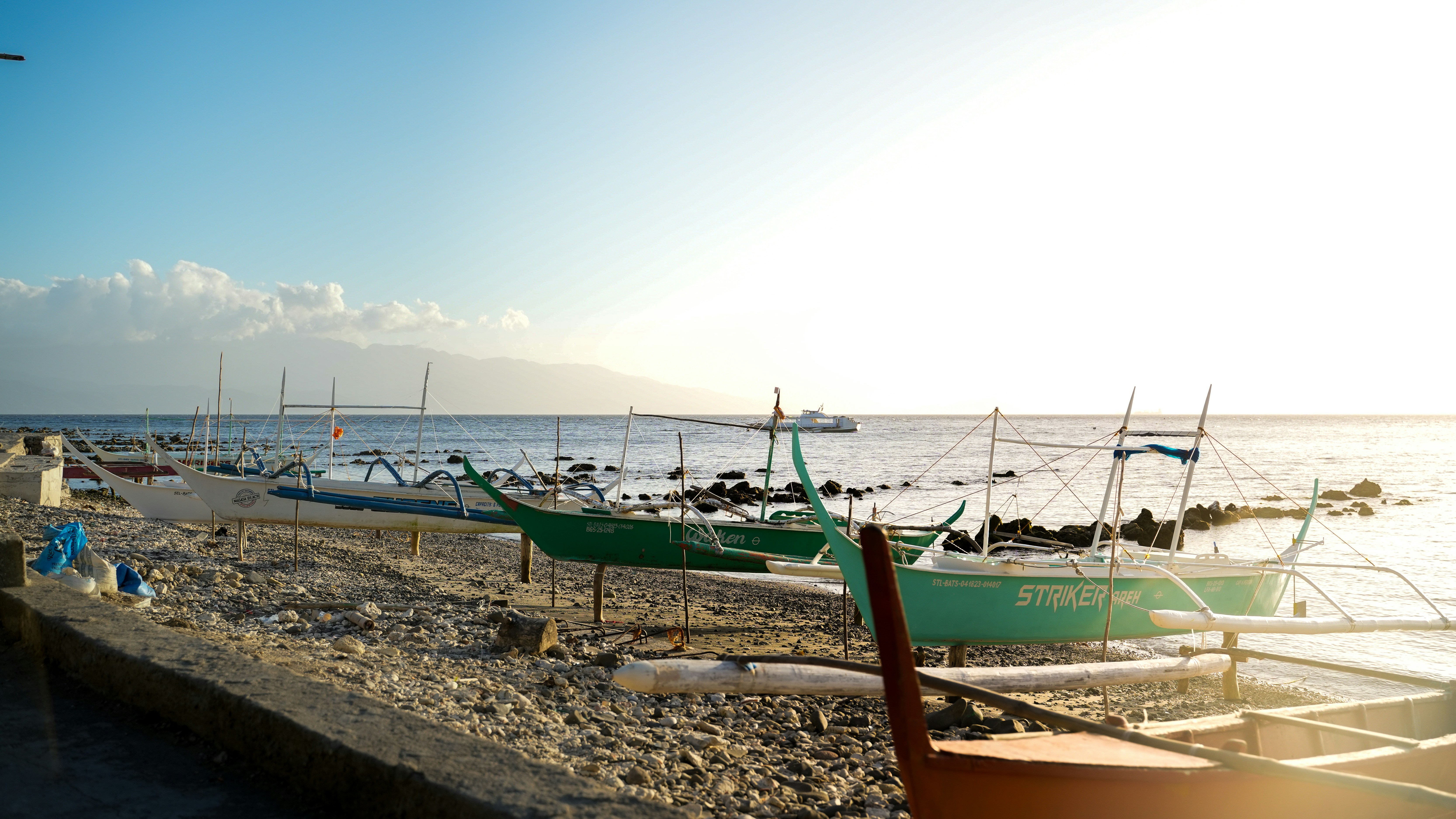 Boats rest on a rocky shore with calm ocean background.