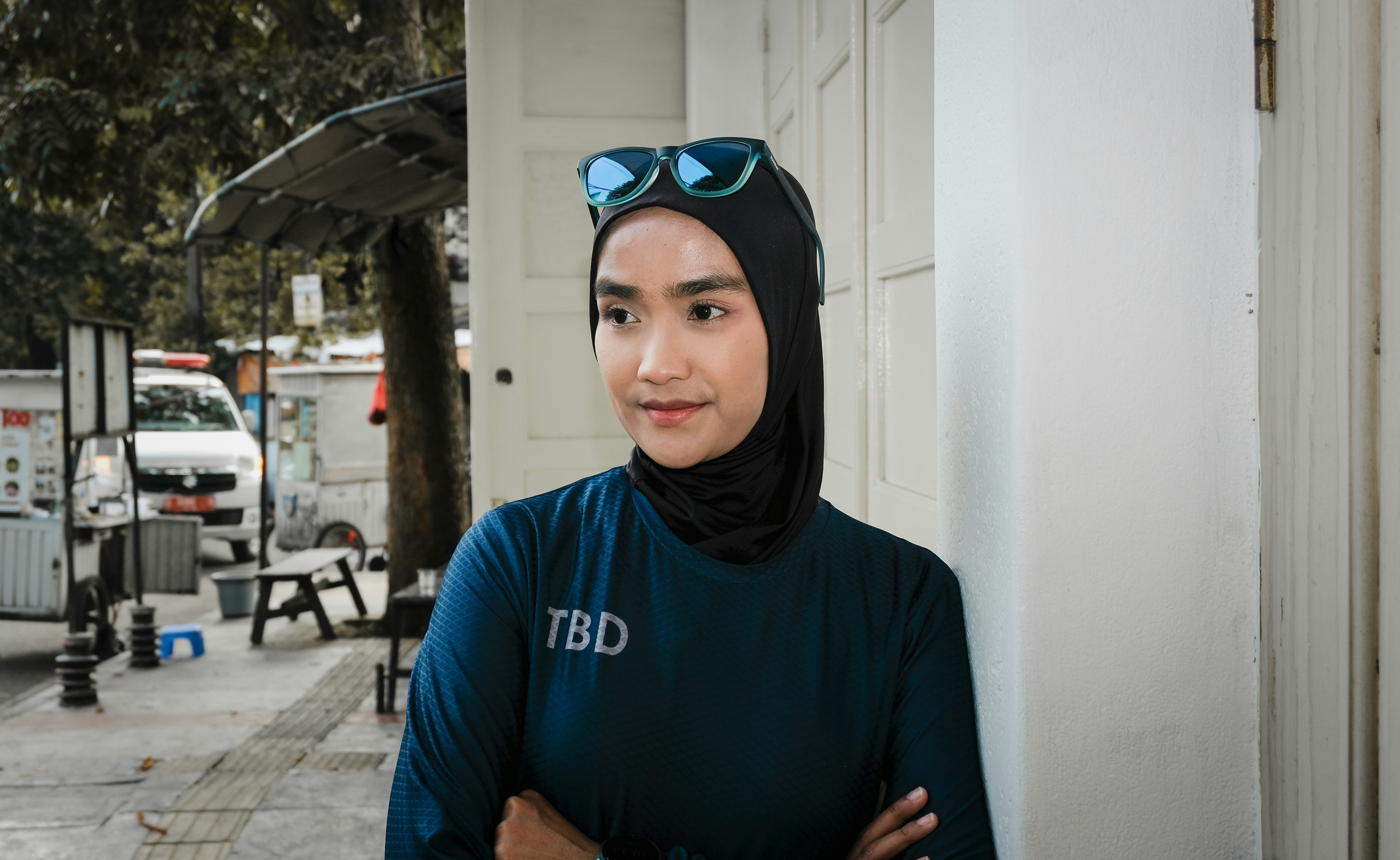 Woman in hijab and sunglasses leans against wall.