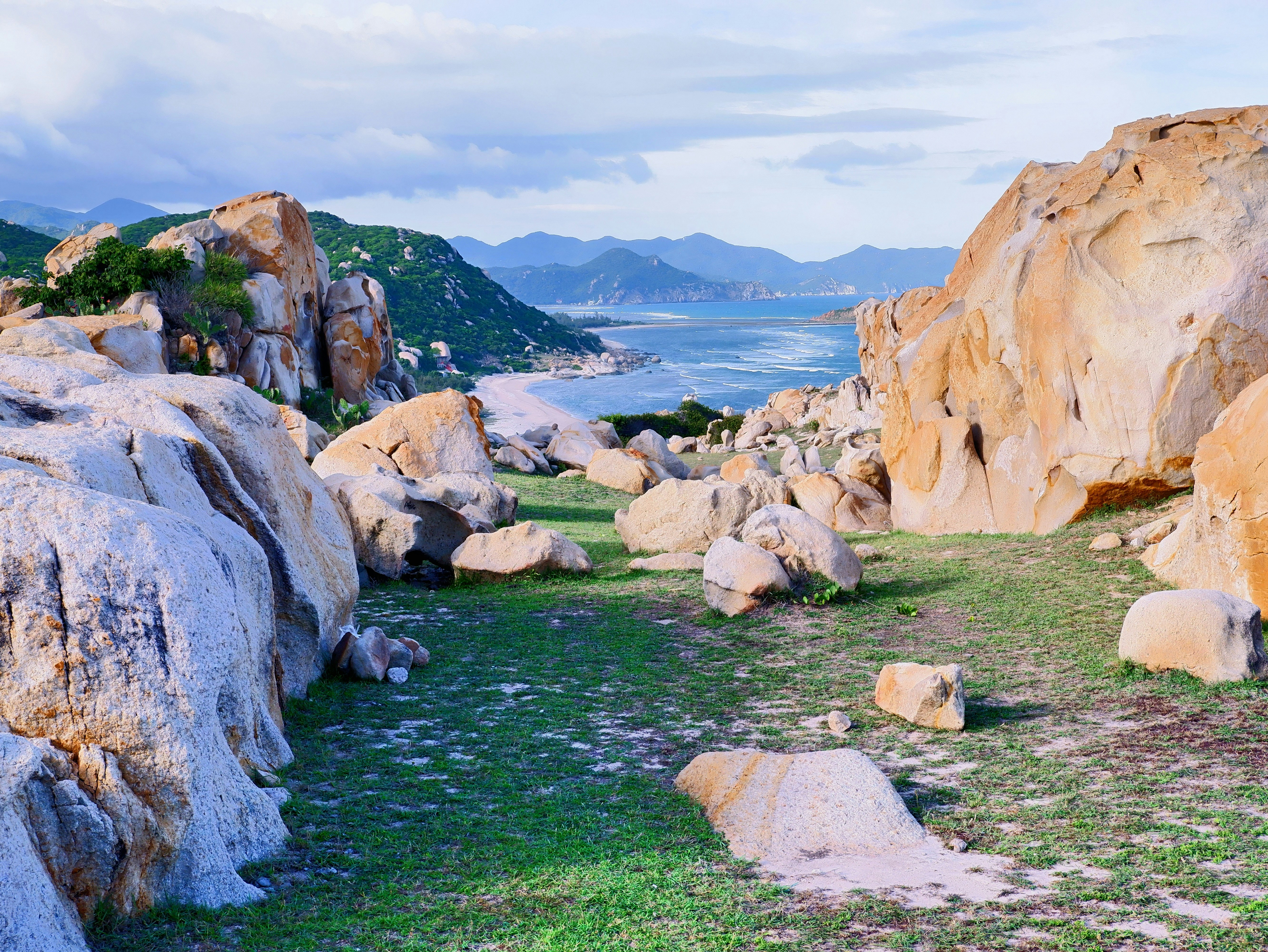 Paisaje costero rocoso con océano y montañas lejanas.