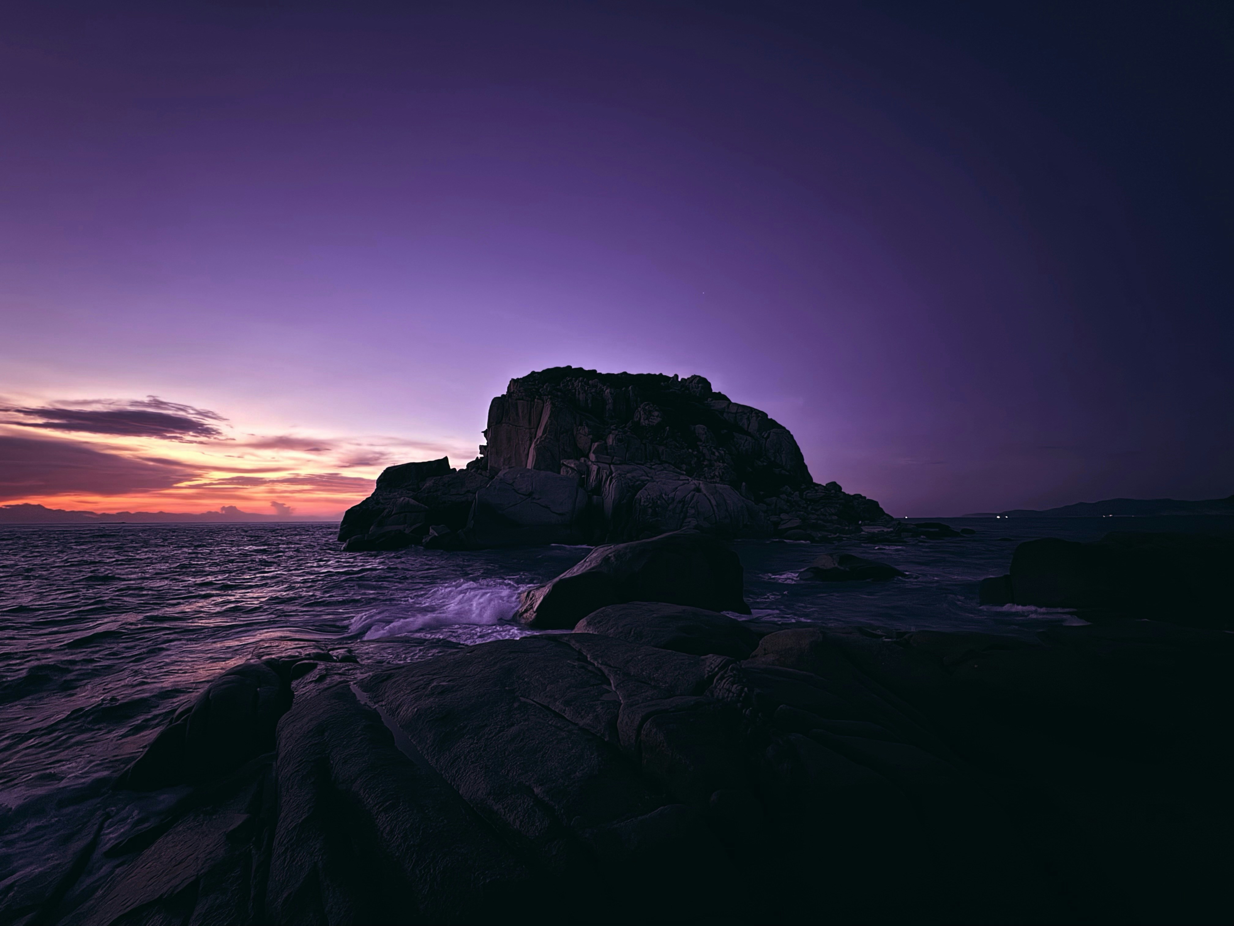 Rocky island silhouette against a vibrant purple sunset