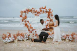 Man proposes to woman on beach with heart decoration.