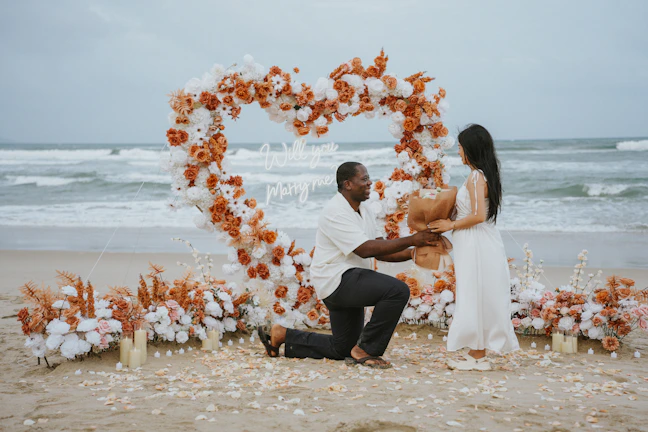 Man proposes to woman on beach with heart decoration.