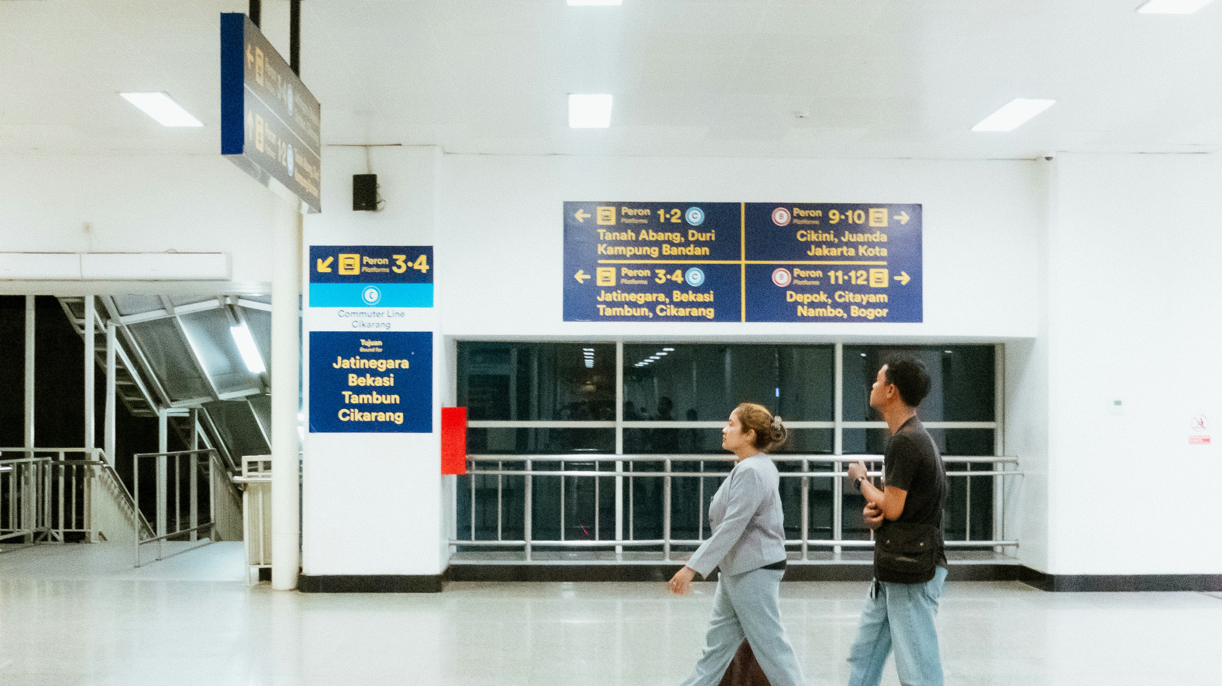 Two people walk past signs in a modern building.
