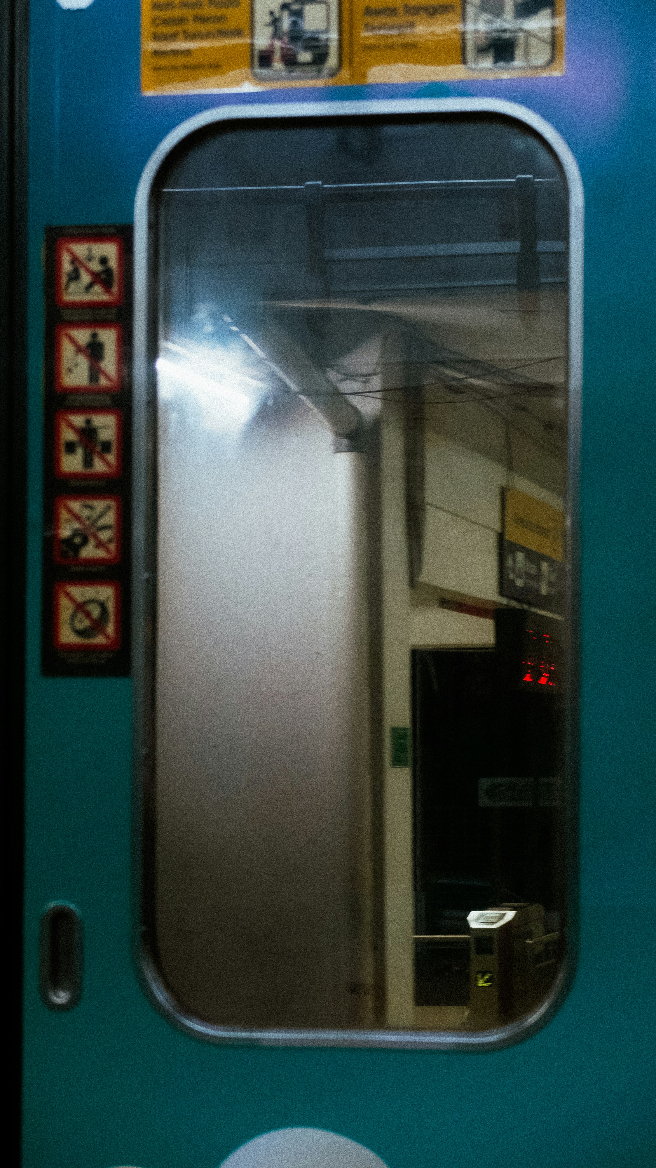 Jendela pintu kereta api yang mencerminkan interior dan tanda peringatan