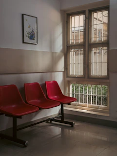 Three red chairs in a waiting room by window