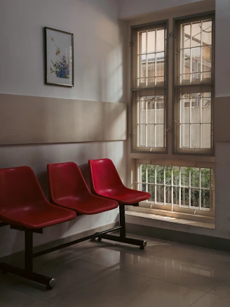 Three red chairs in a waiting room by window