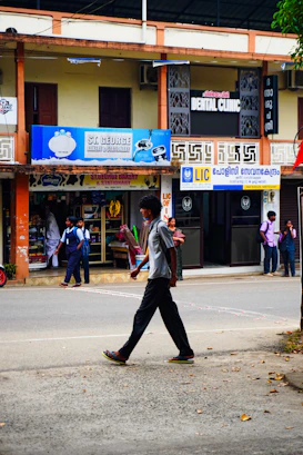 Man walking across a street in front of shops.