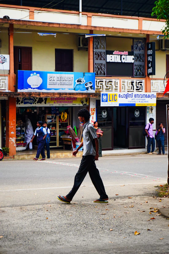 Man walking across a street in front of shops.