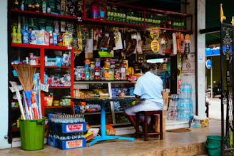 Man sits at a small table outside a well-stocked store
