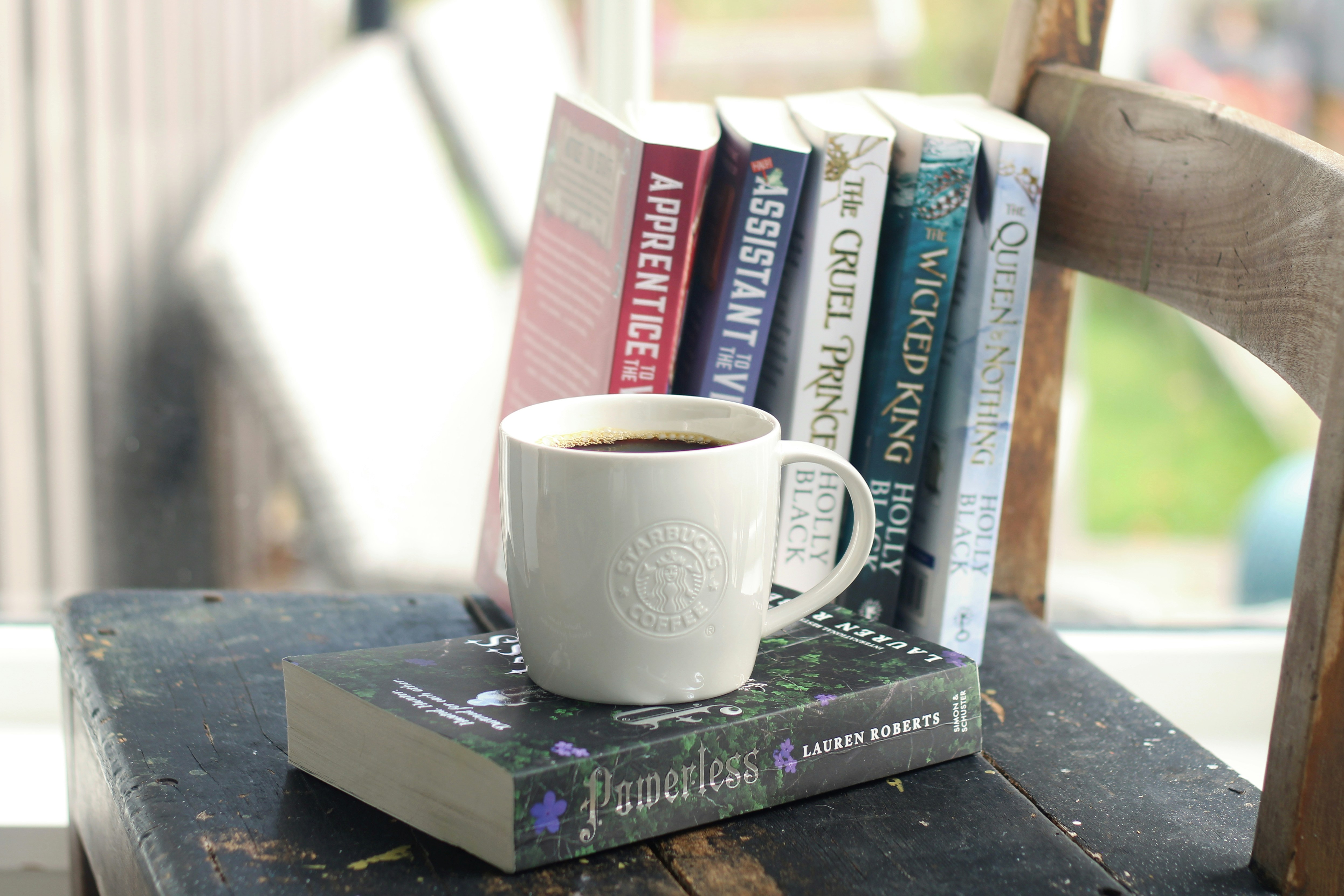 Une tasse de café repose sur des livres près d’une fenêtre.