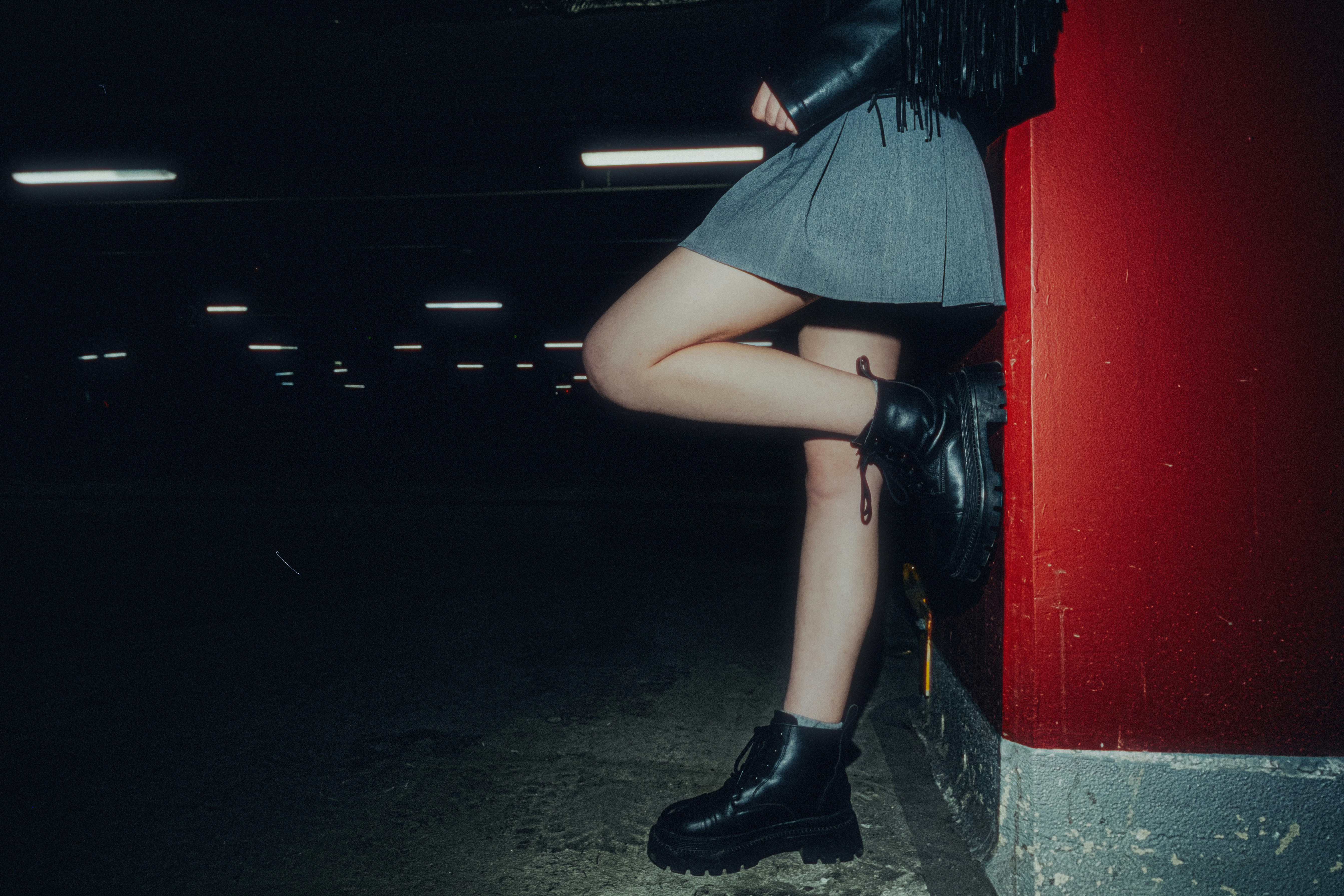 Woman in skirt and boots leaning against red wall
