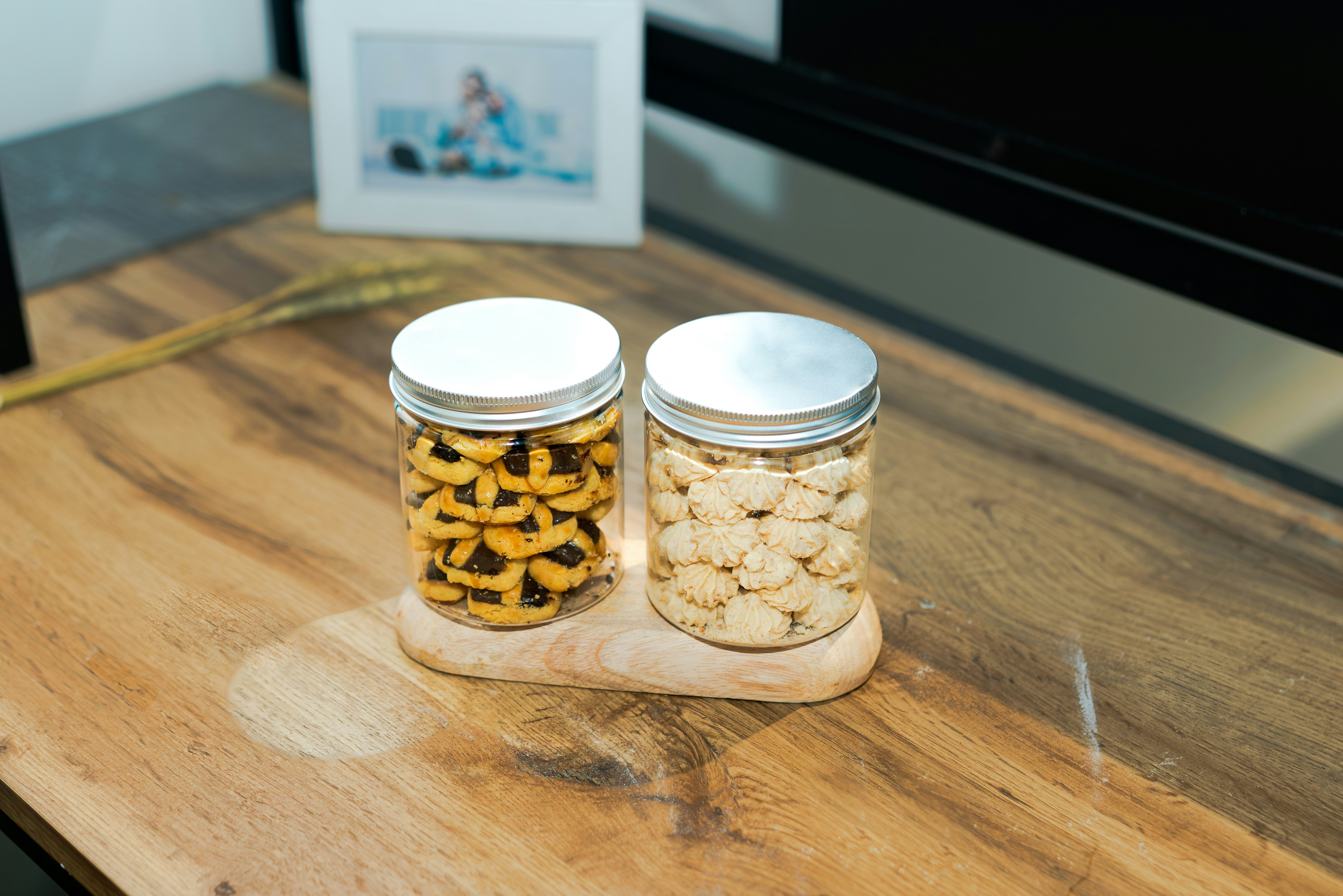 Two jars of cookies on a wooden stand.