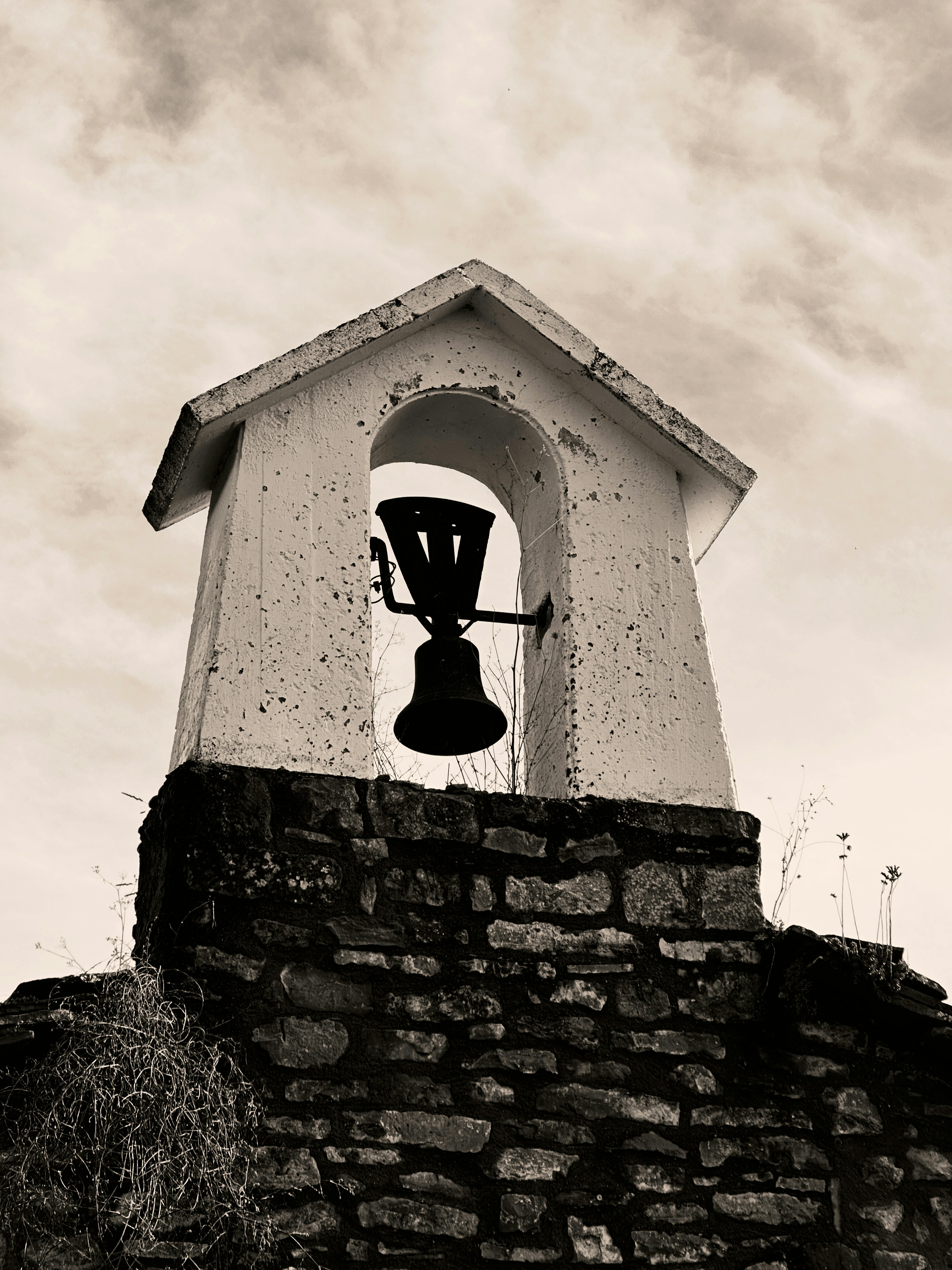 A bell tower with a bell against a cloudy sky