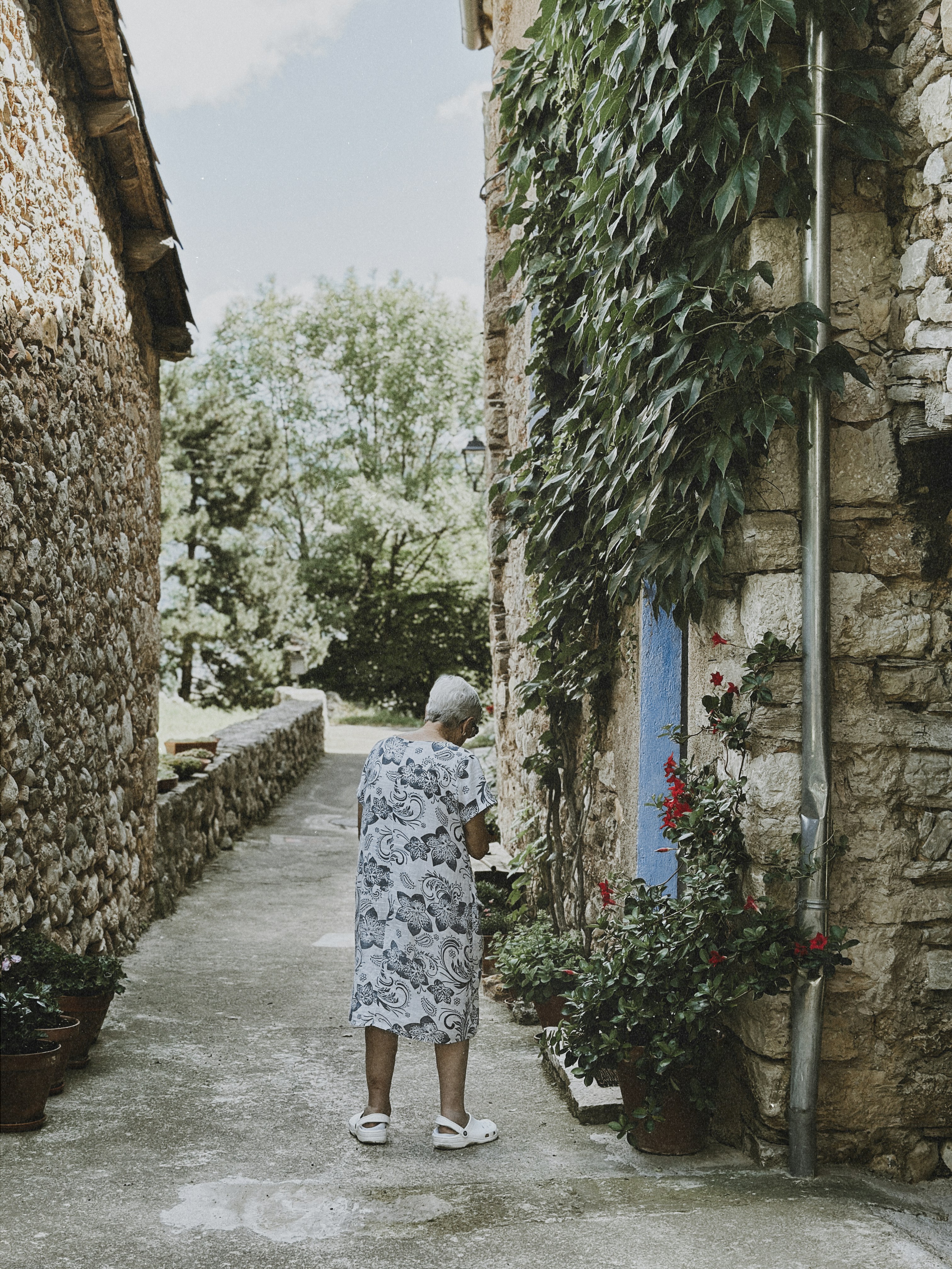 Elderly person walks down a narrow stone alley.