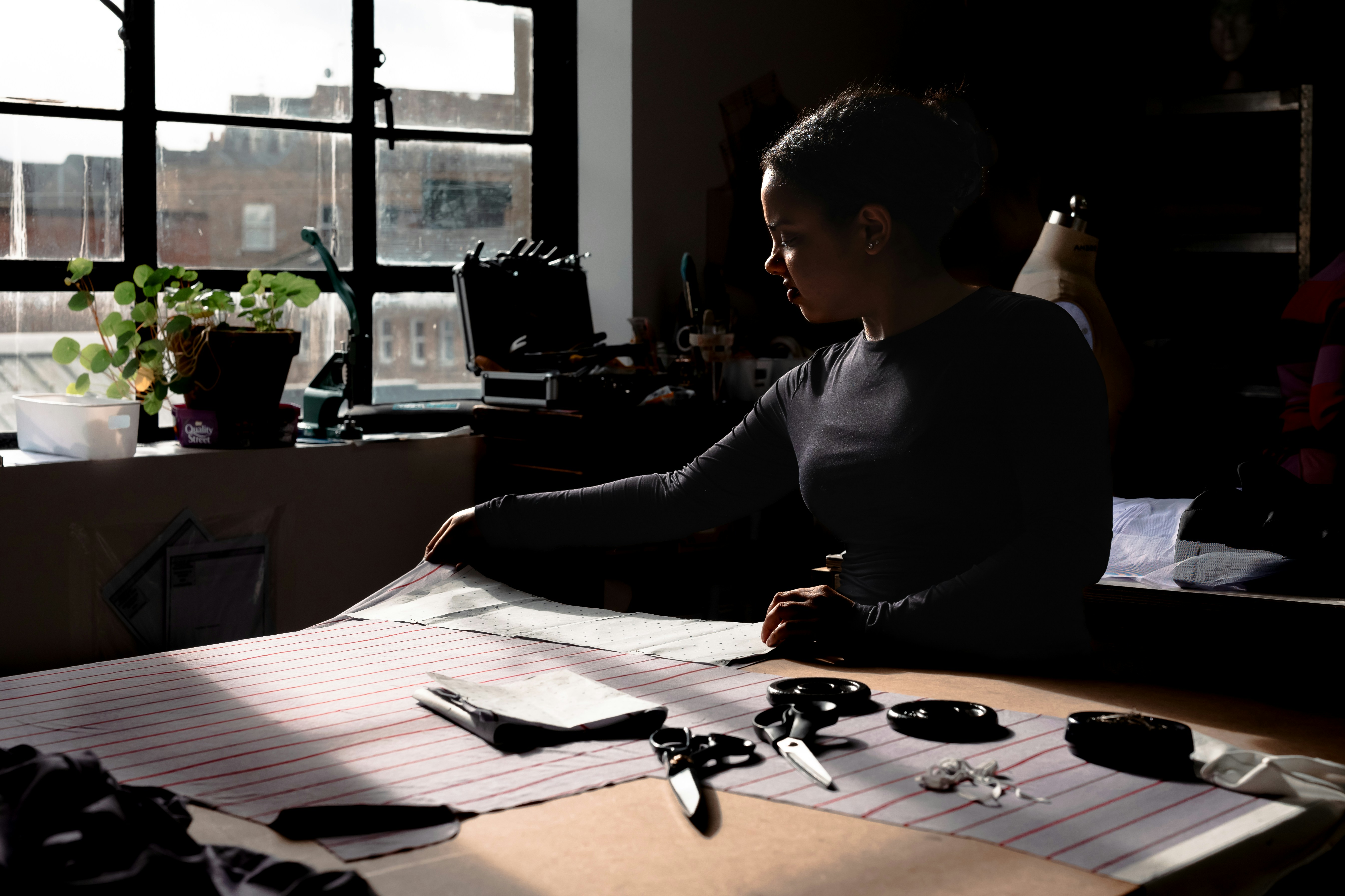 Woman working on a large paper with scissors and tools.