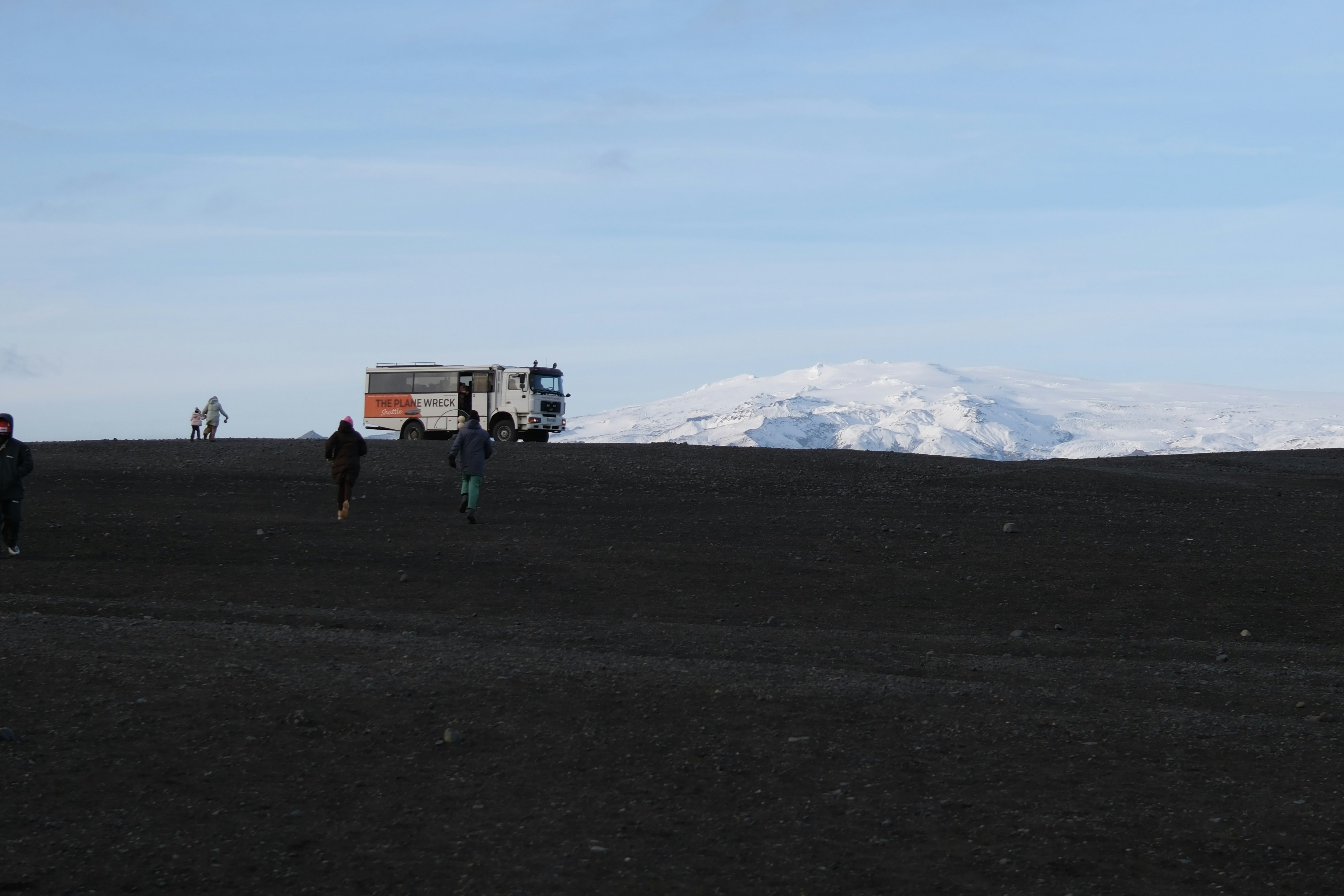 Gente corriendo en una playa de arena negra con autobús y nieve