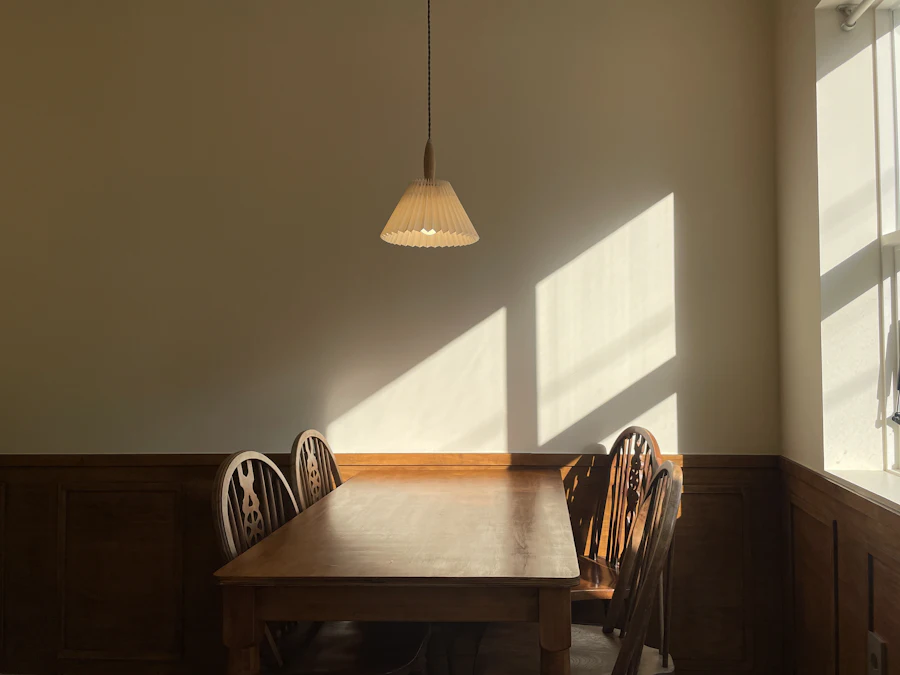 A wooden dining table and chairs, with patches of low sun on the wall behind