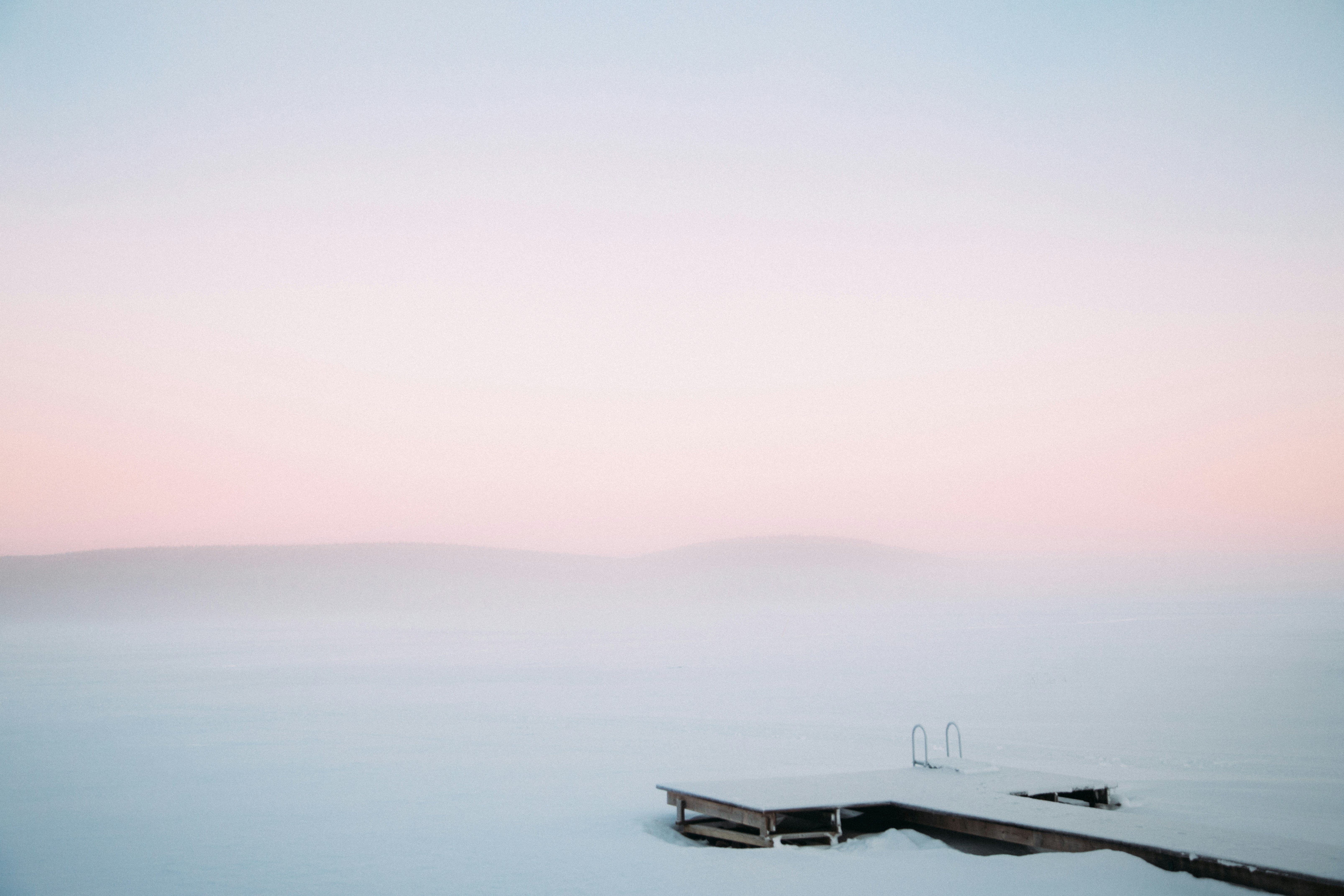 Holzsteg an einem gefrorenen, nebligen See bei Tagesanbruch