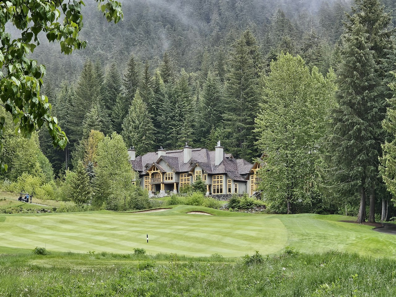 Lodge-style home beside a golf course, framed by dense evergreen forest.