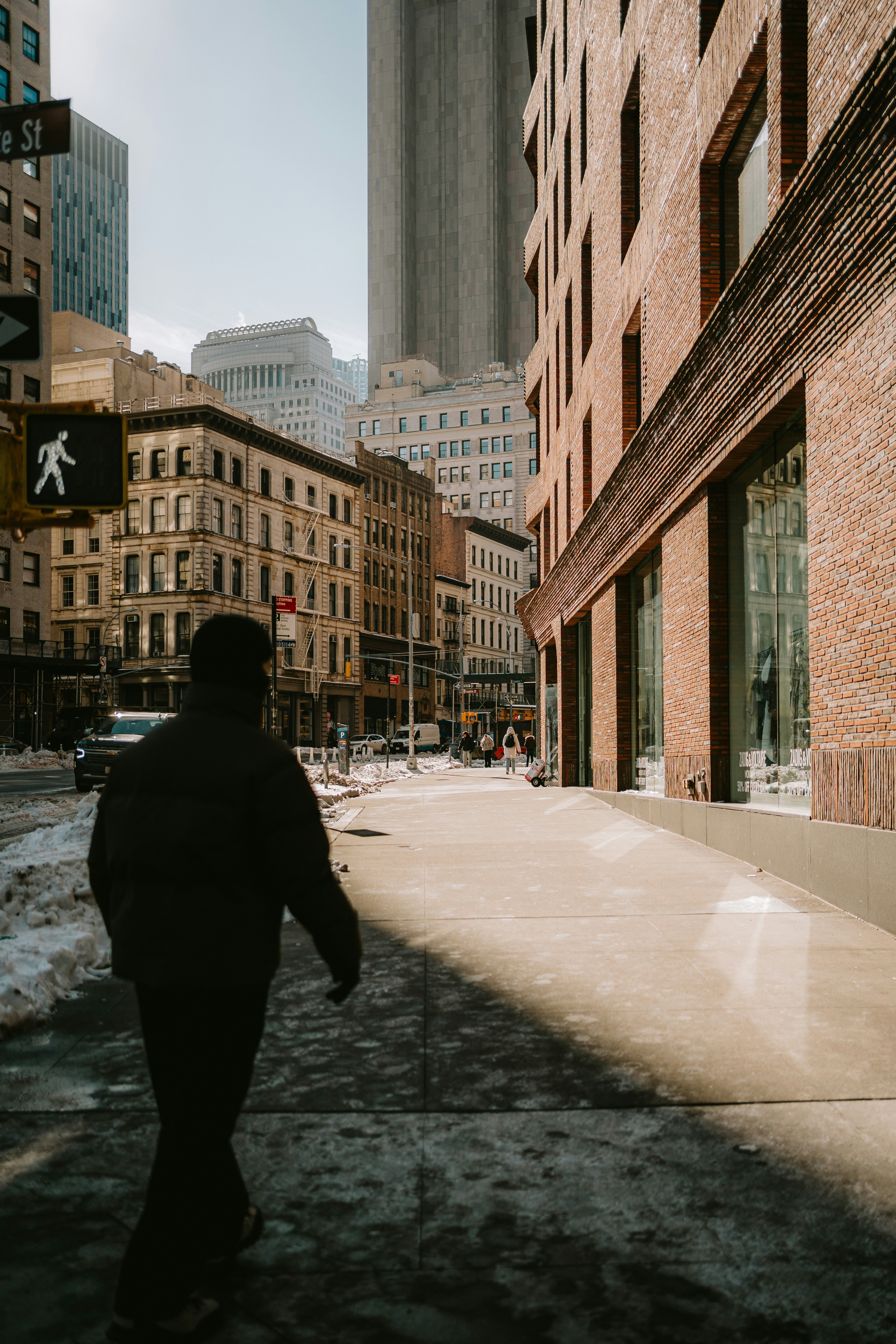 A person walks down a sunny city street in winter.