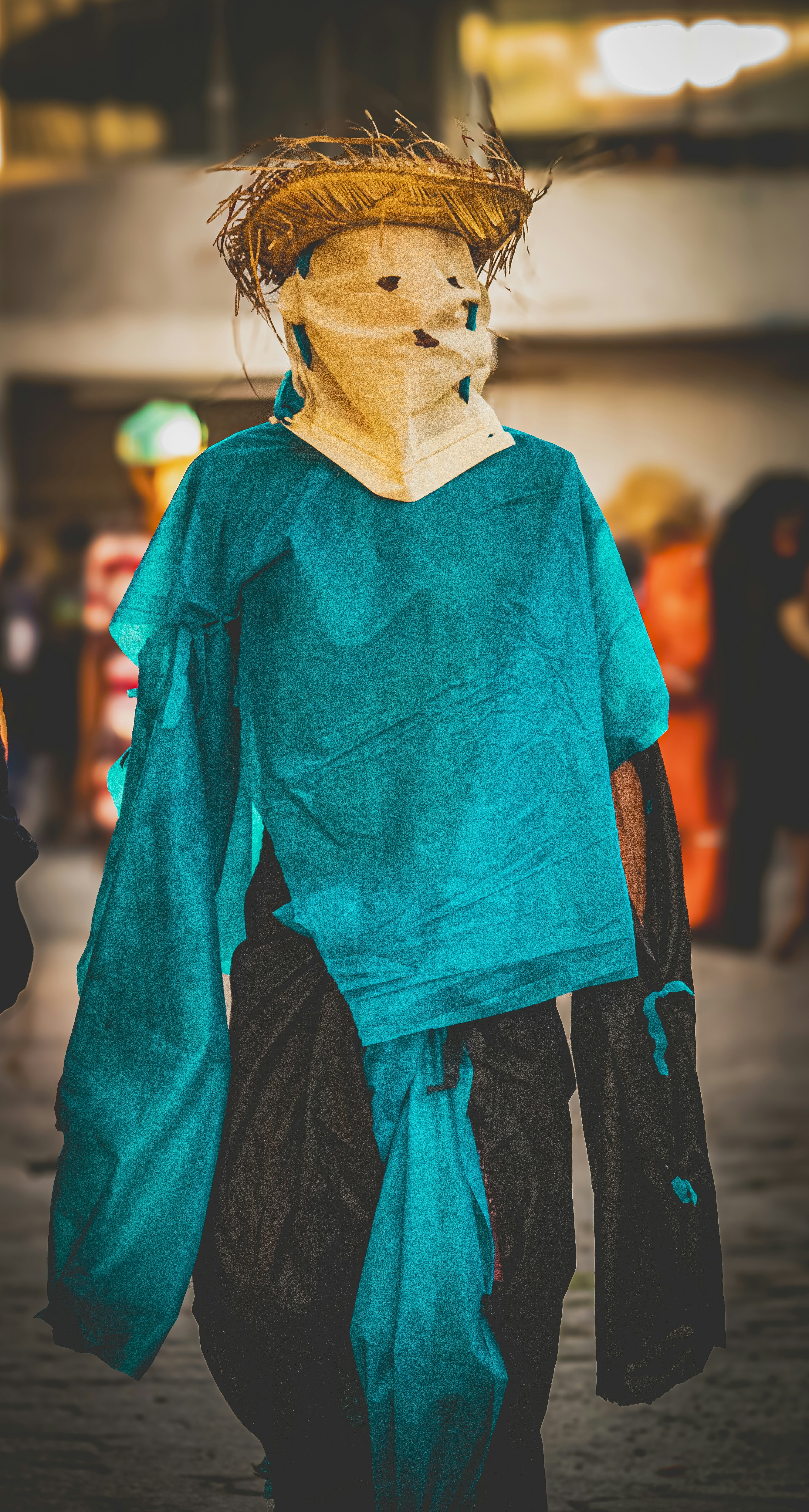Eine Person mit Strohhut und türkisfarbenem Kostüm geht nach vorne