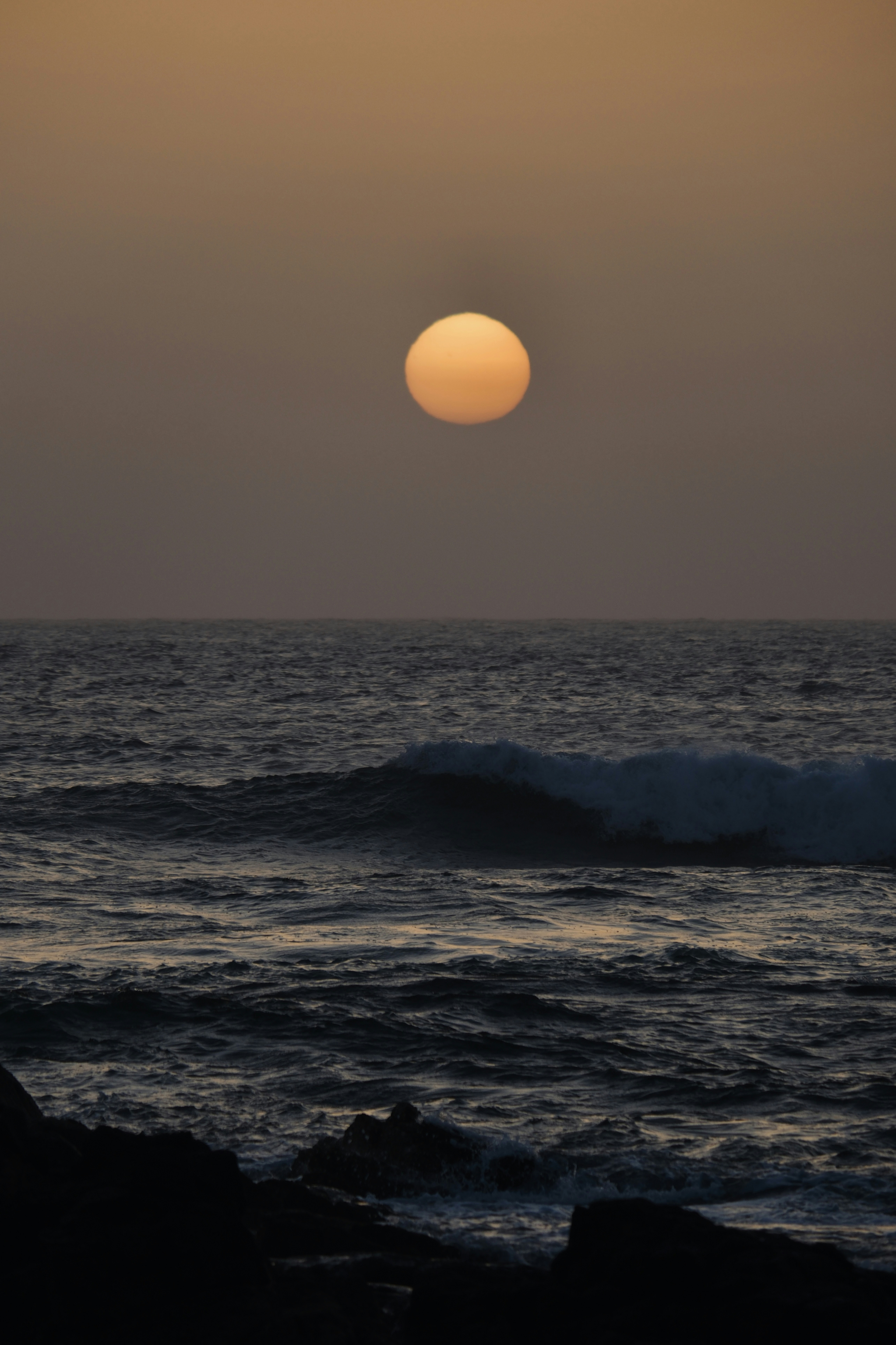 A large orange sun setting over a dark, choppy ocean.