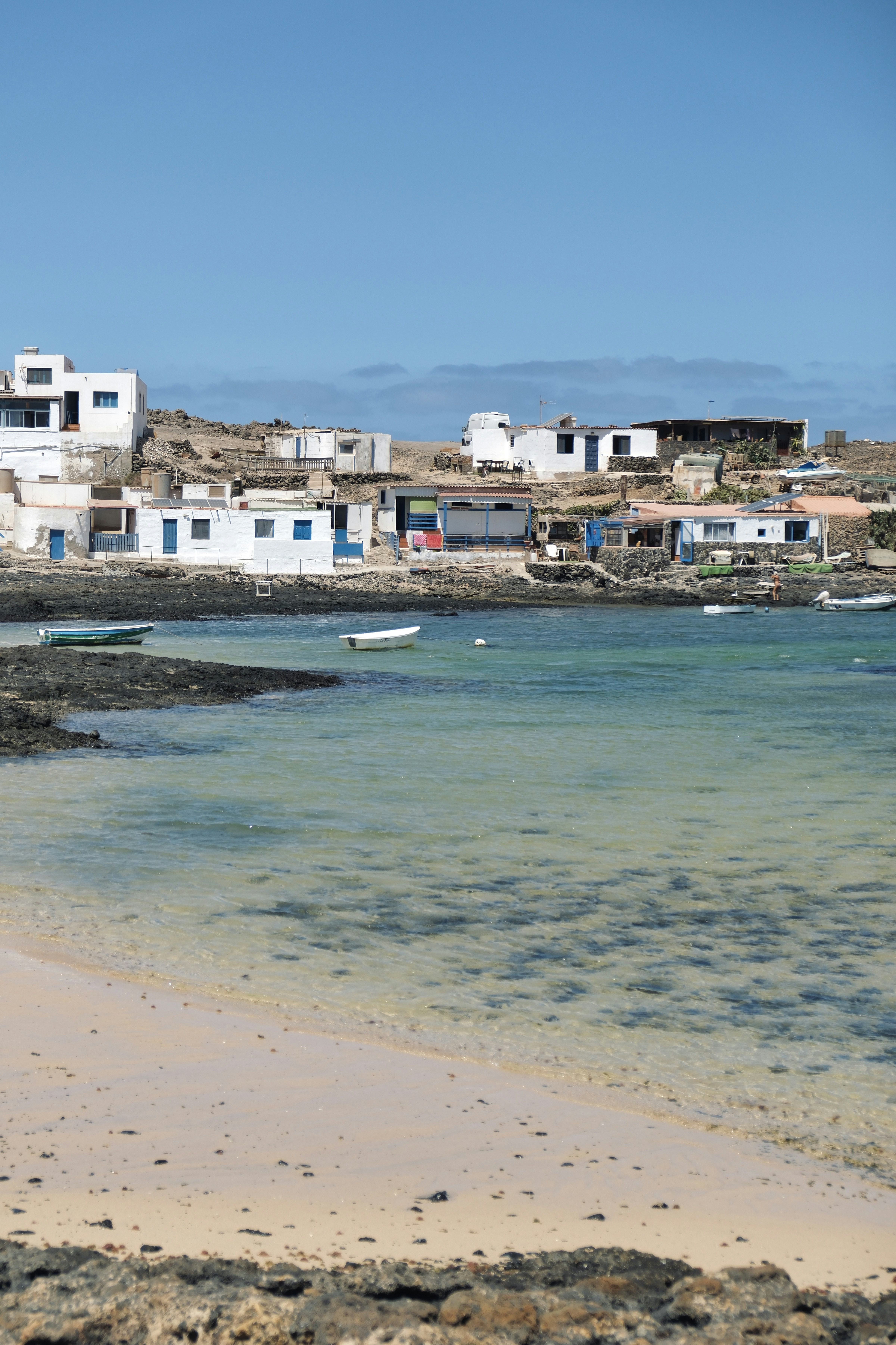 Small white buildings line a rocky shore with boats.
