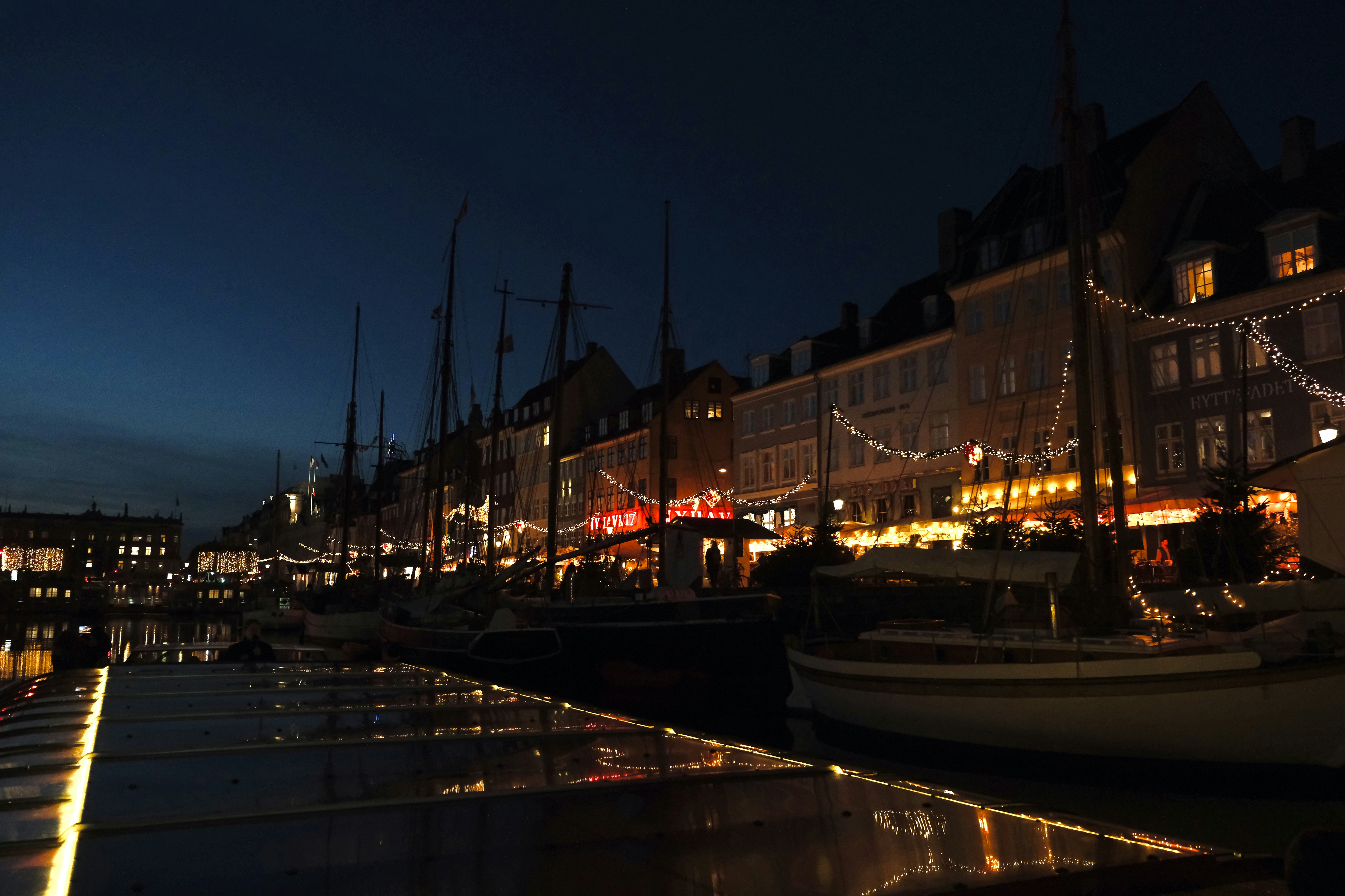 Boats docked in a harbor at night with lit buildings.