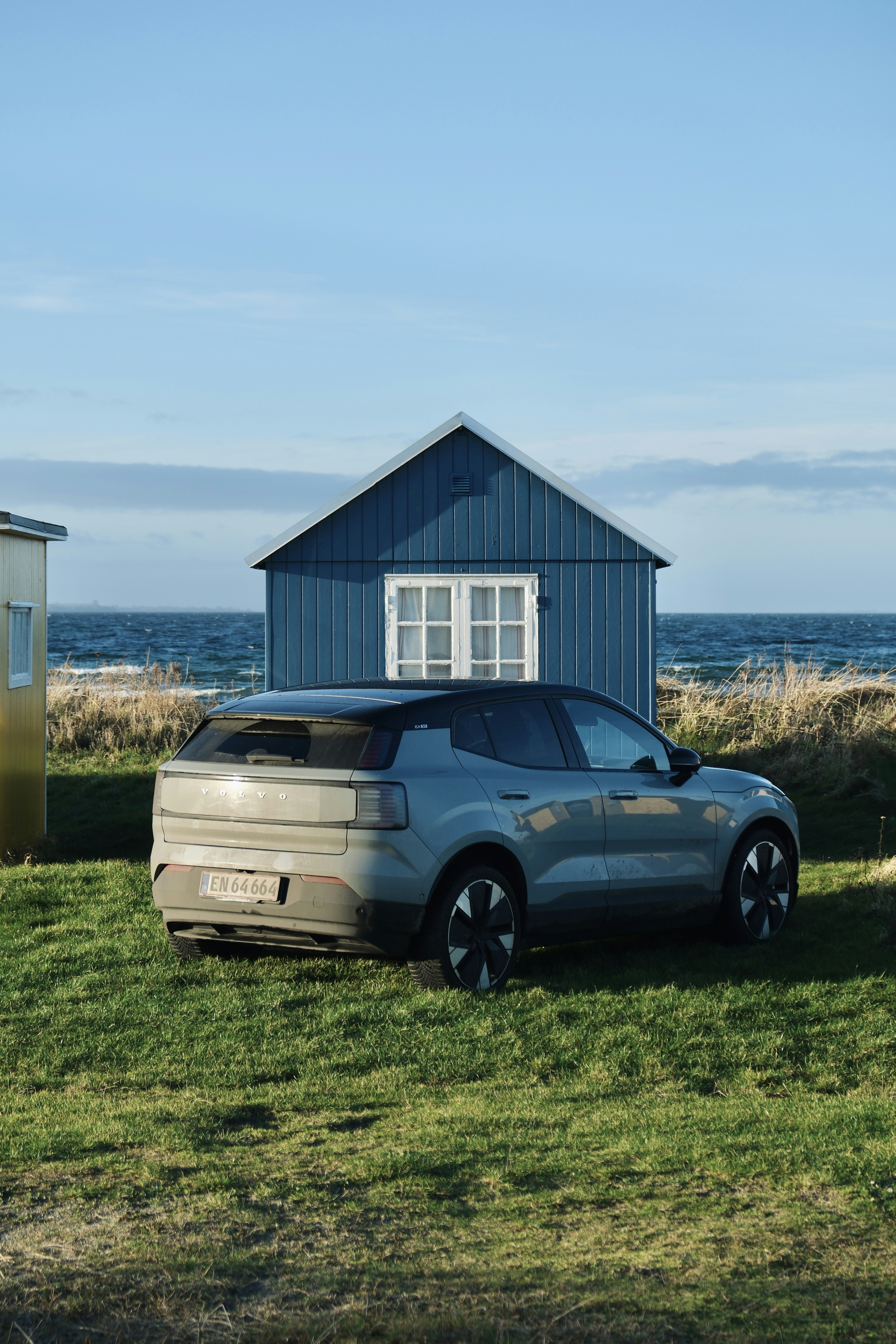 A modern car parked by a blue beach house.