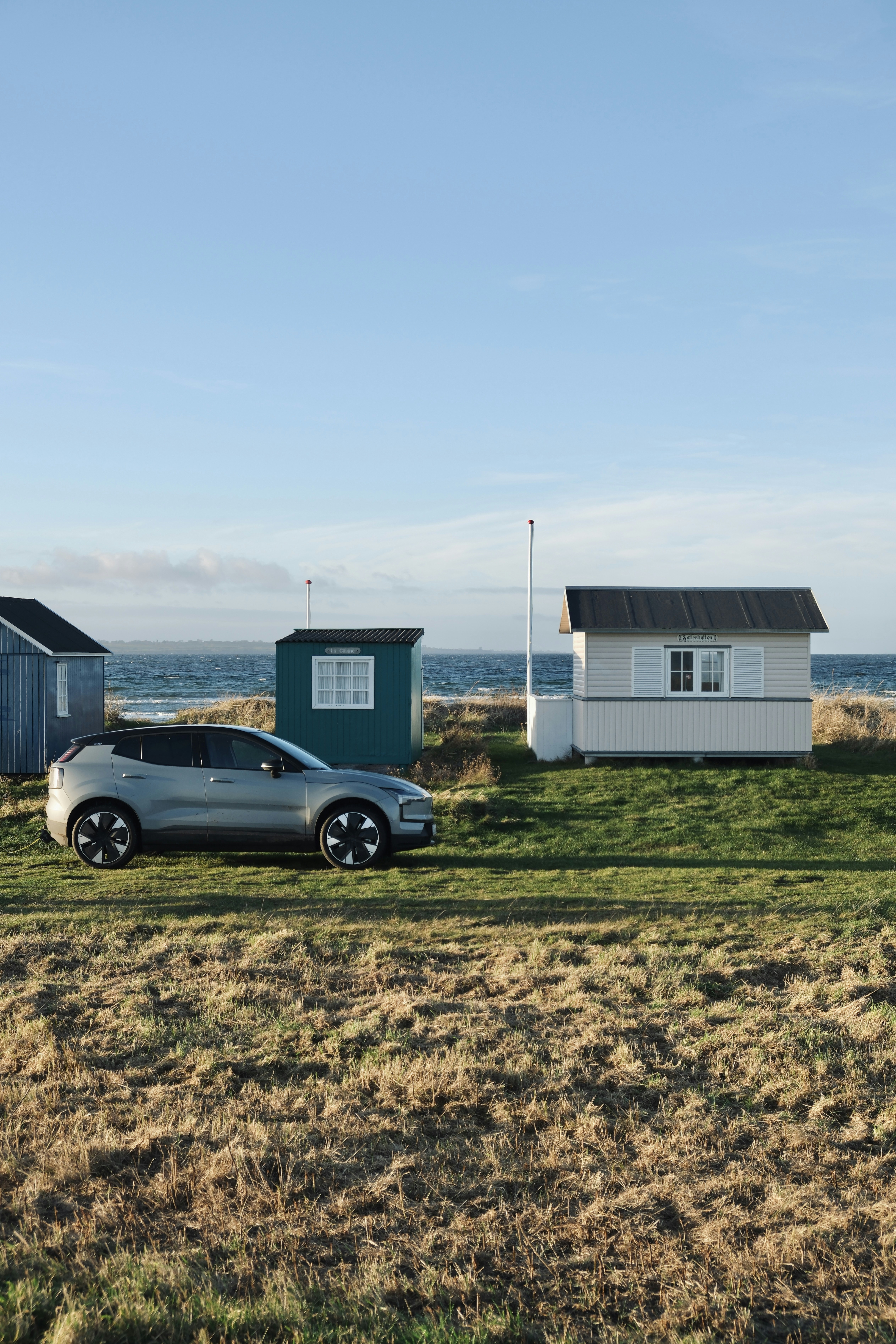 Silver car parked near beach huts by the ocean