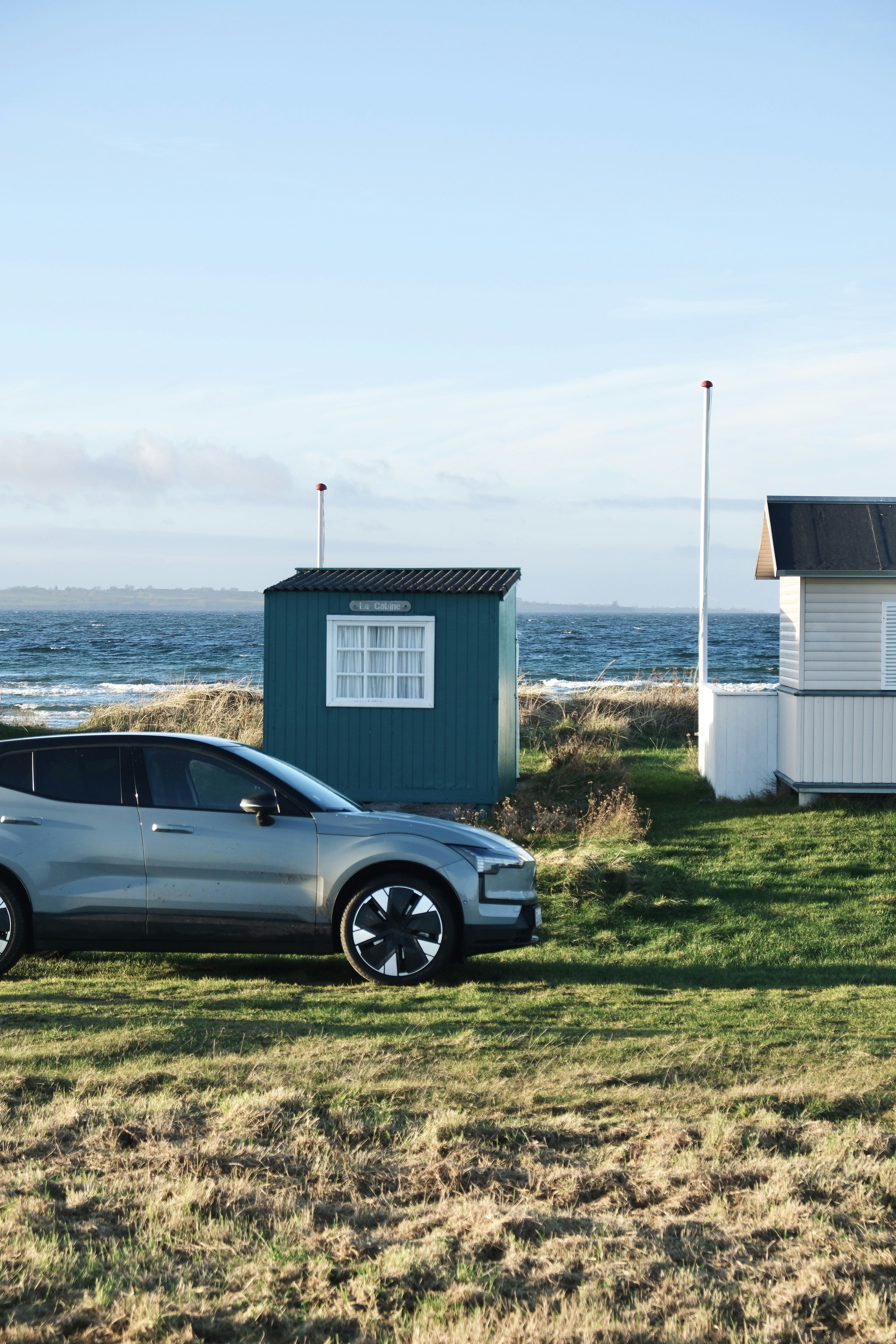 Silver electric car parked by beach huts