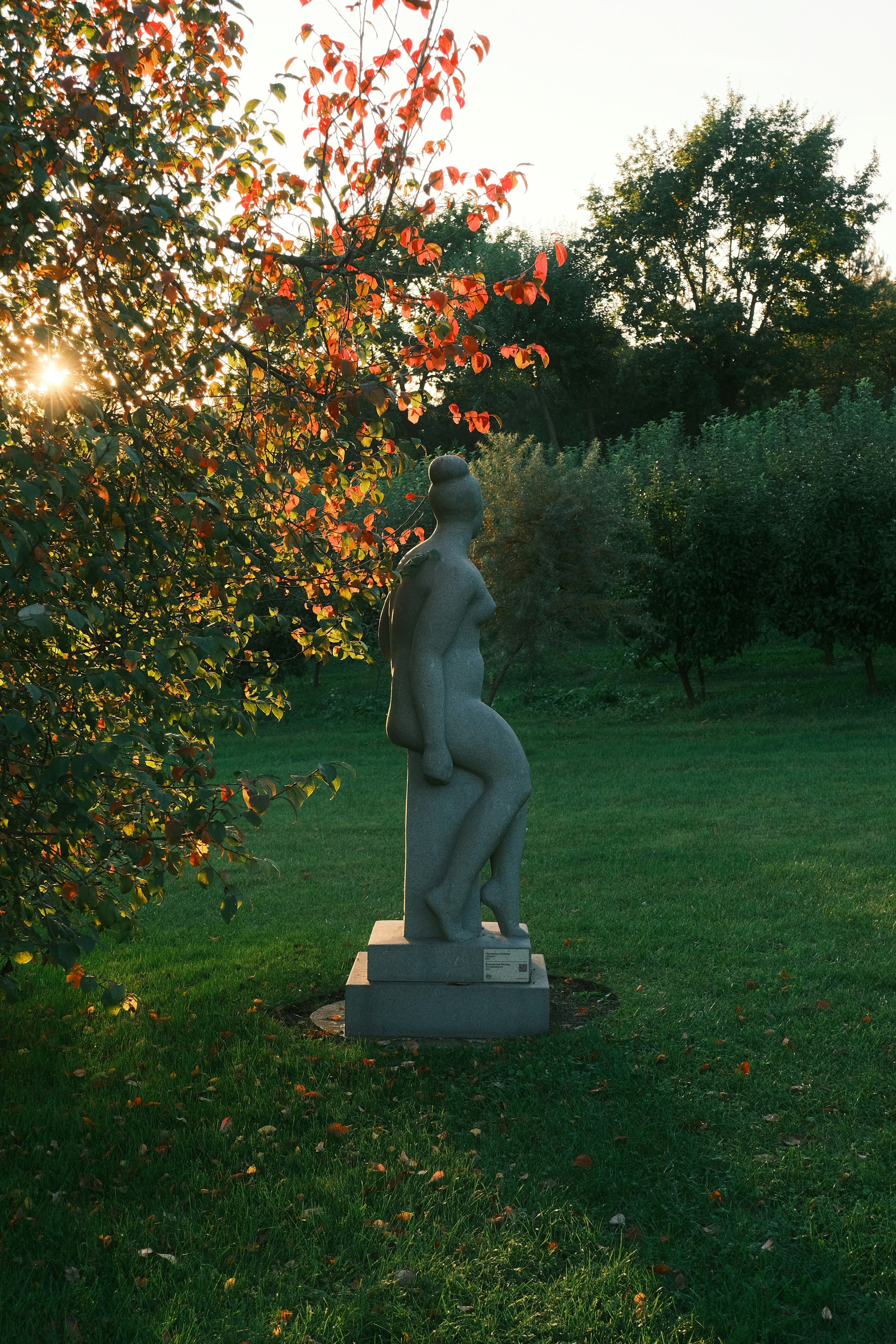 Stone sculpture in a sunlit park with autumn leaves.