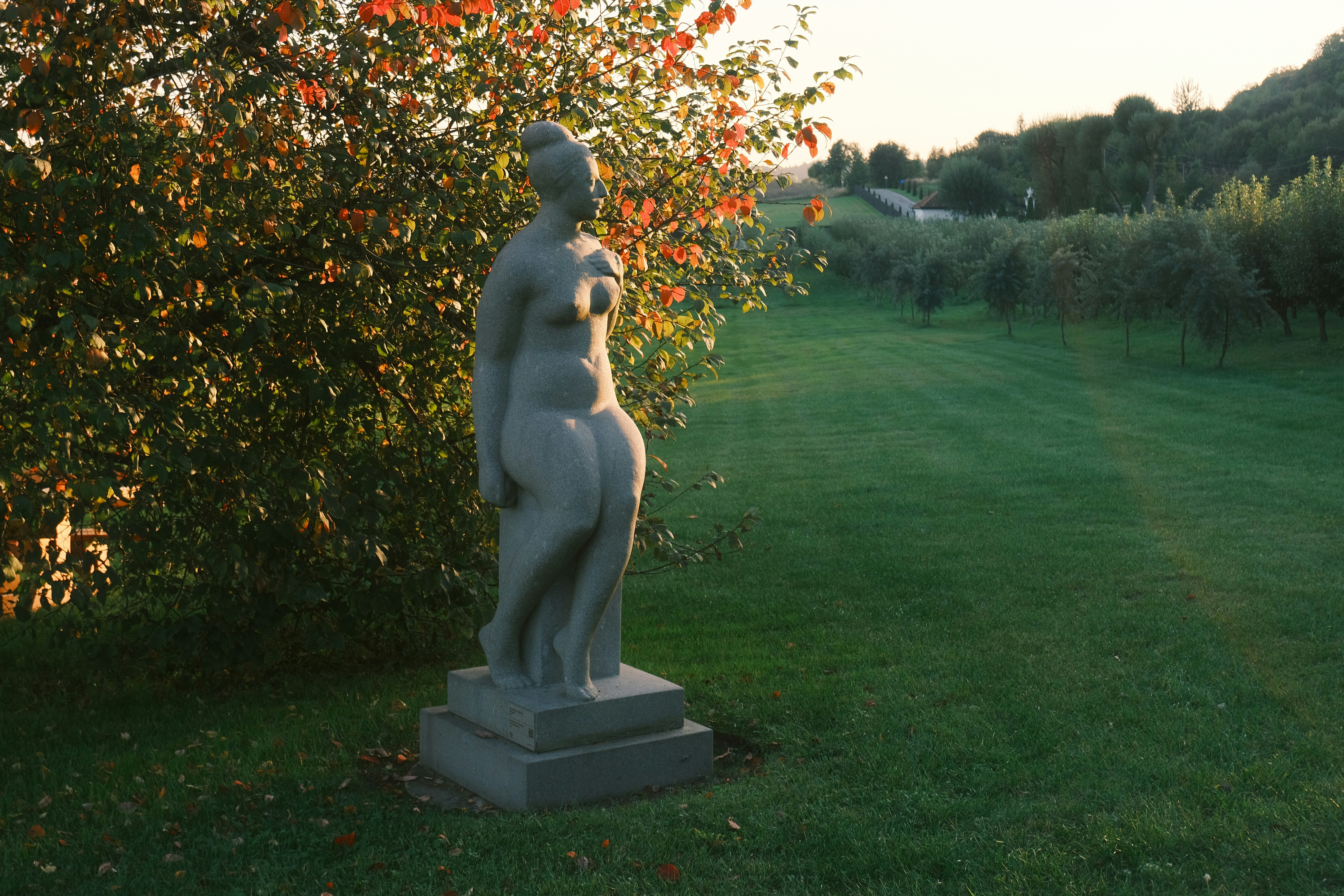 A stone statue of a woman in a grassy field.