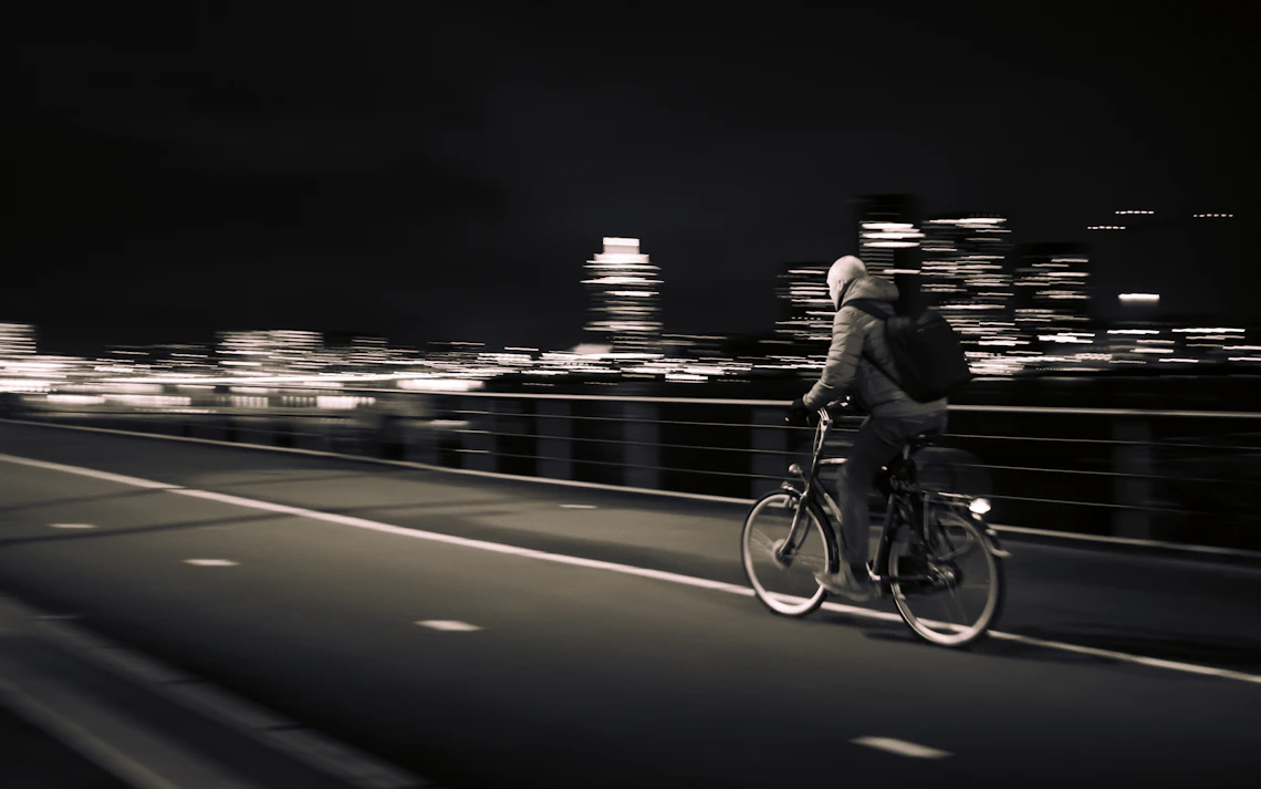 Cyclist riding across an illuminated urban bridge at night