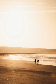 Two people walking on a beach at sunset