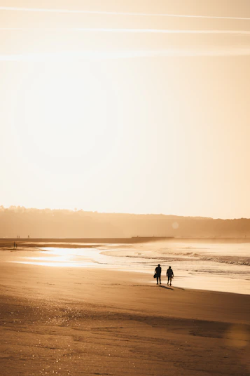 Two people walking on a beach at sunset