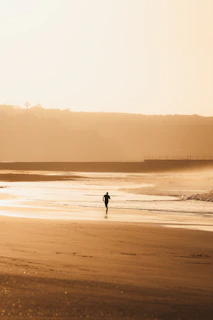 A lone figure jogs on a sandy beach at sunset.