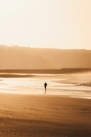A lone figure jogs on a sandy beach at sunset.